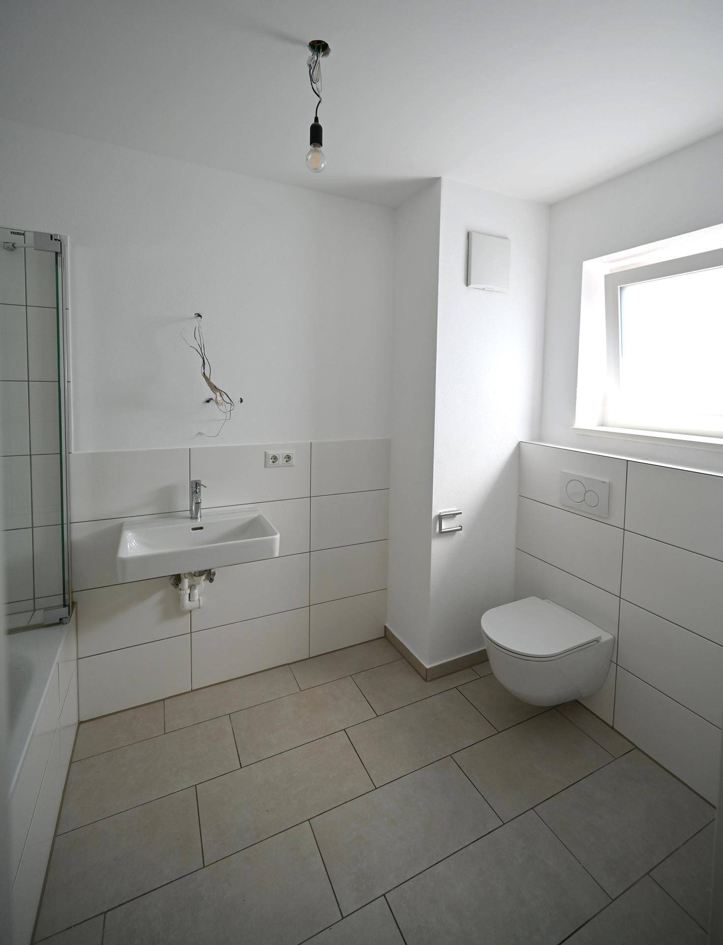 Helles Badezimmer mit WC, Waschbecken und Fenster, ausgestattet mit modernen weißen Fliesen.