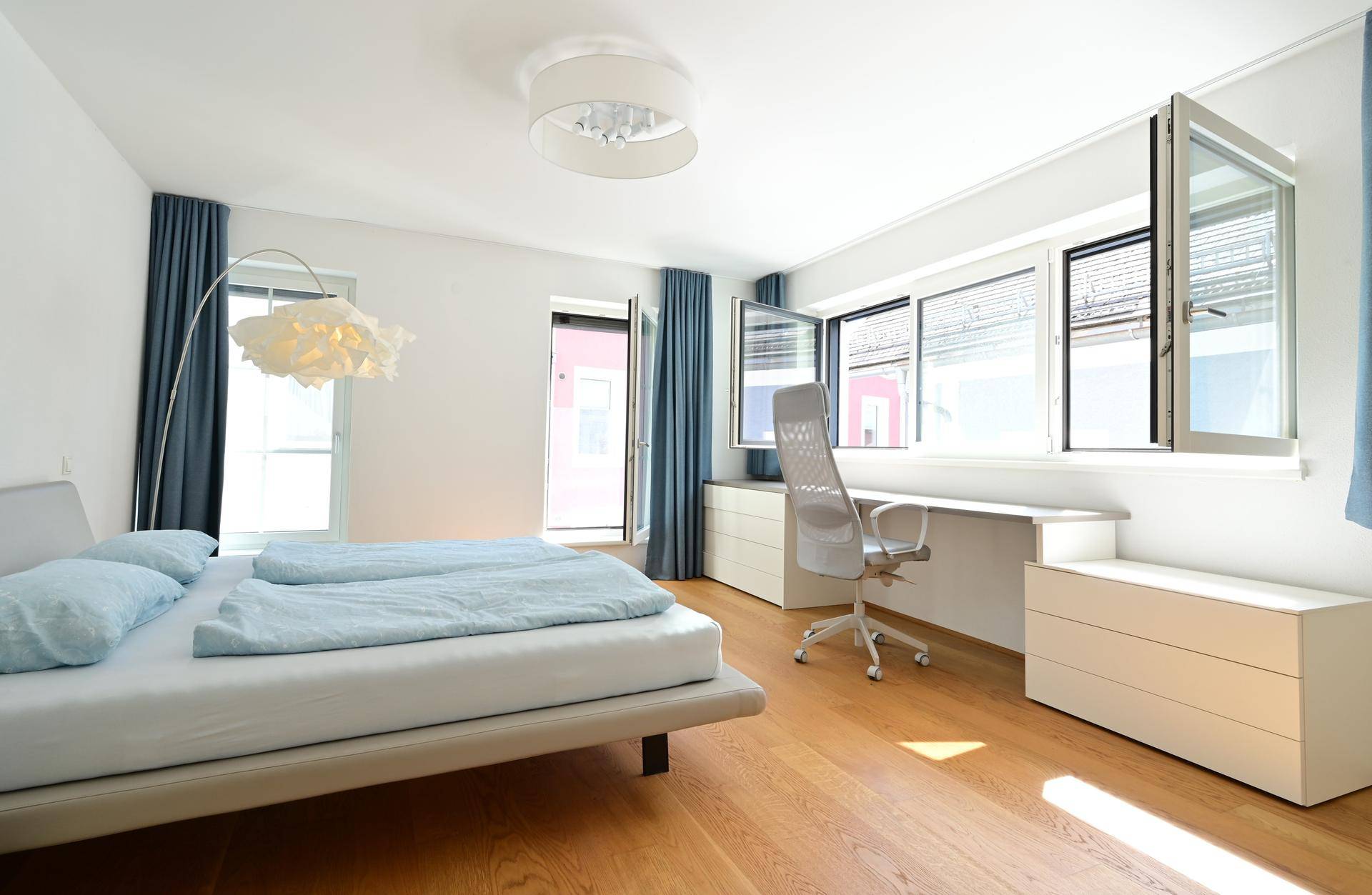 Geräumiges Schlafzimmer mit Holzboden, großen Fenstern und moderner Einrichtung für eine angenehme Atmosphäre.