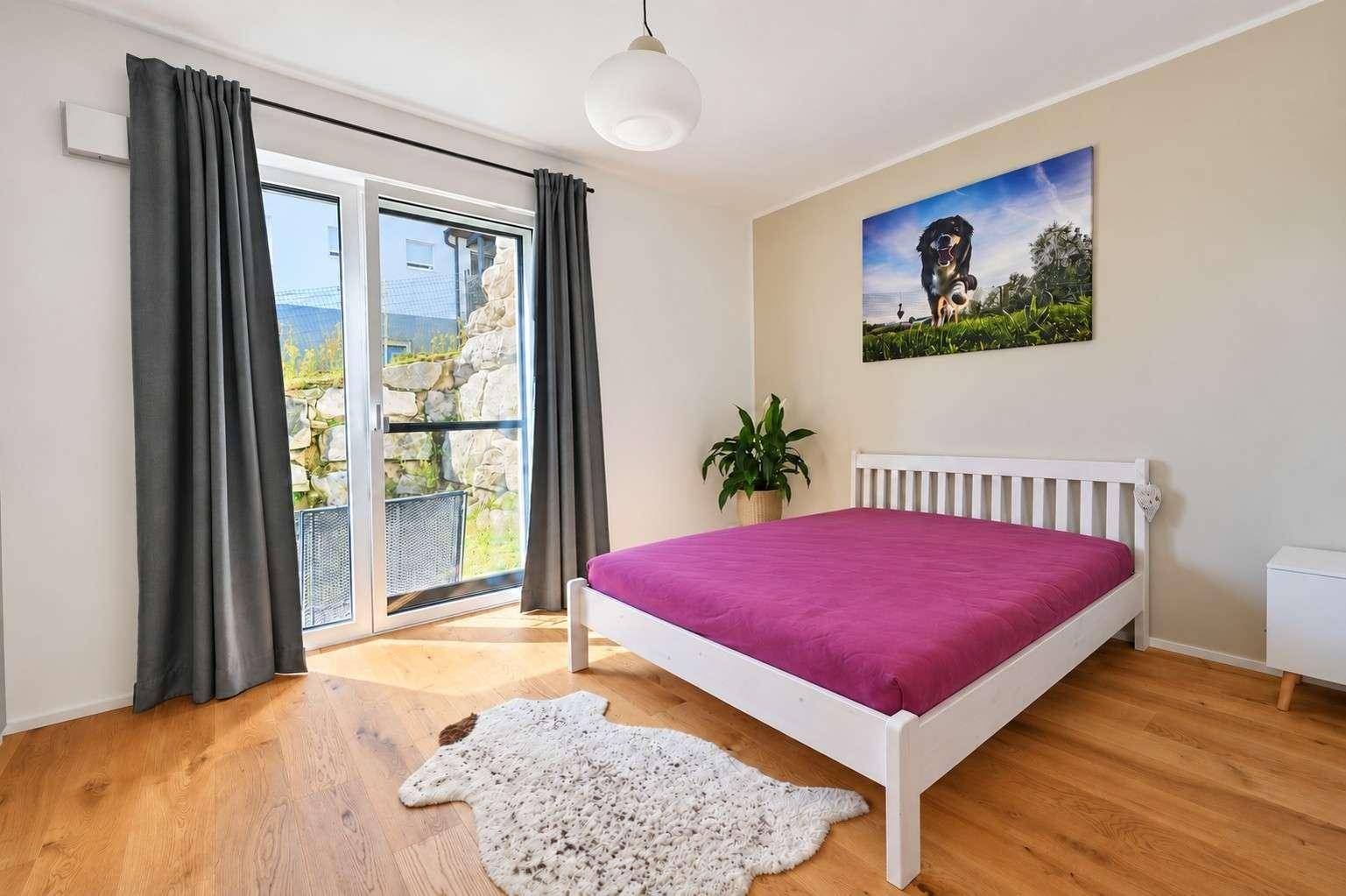 Helles Schlafzimmer mit Holzboden, weißem Bett und Zugang zu einem Außenbereich.
