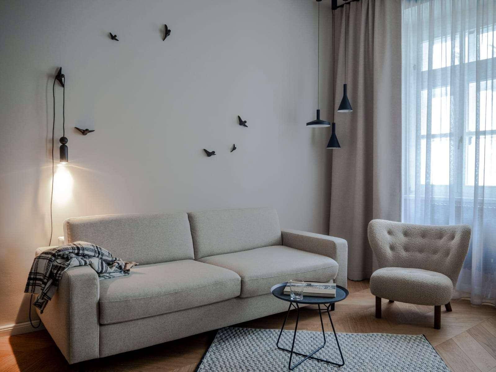 Gemütliches Wohnzimmer mit hellem Sofa, Sessel und dekorativer Wandbeleuchtung.