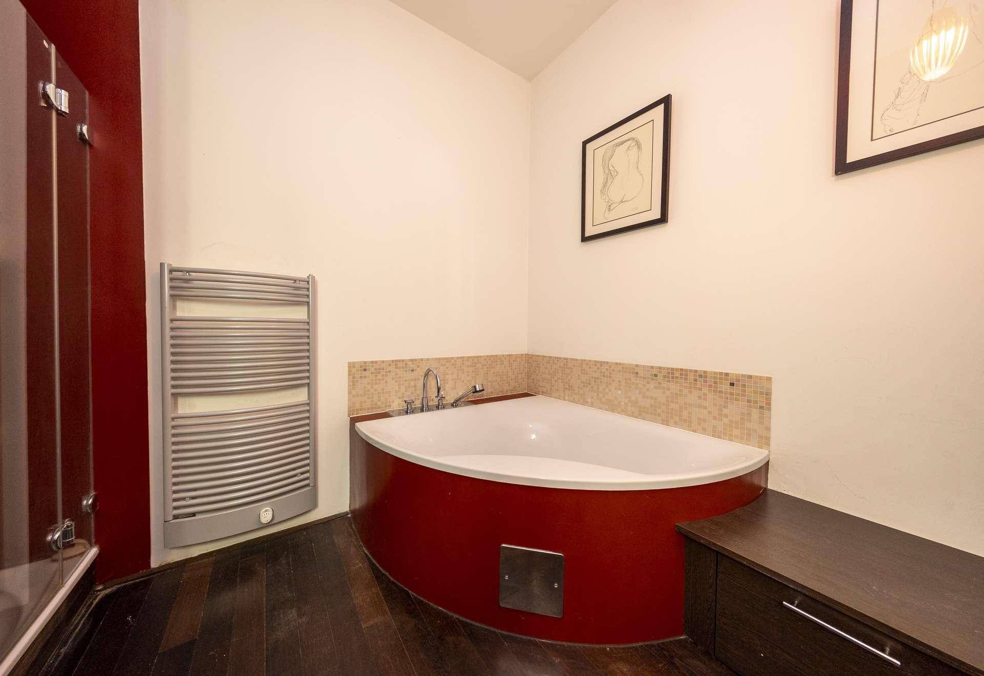 Badezimmer mit roter Eckbadewanne und beheiztem Handtuchhalter, dunkler Holzboden.