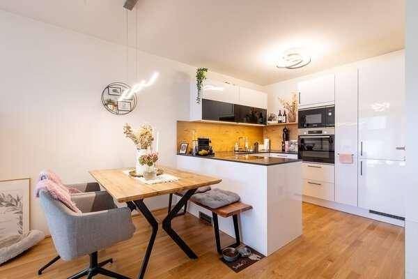 Moderne Einbauküche mit weißen Hochglanzfronten, Kochinsel und Essbereich.