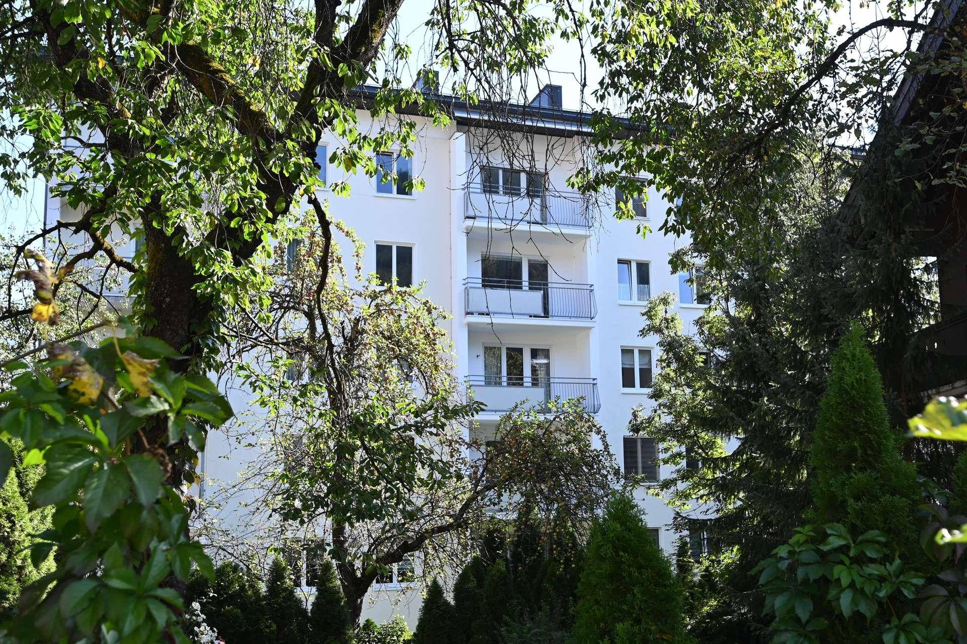 Mehrfamilienhaus mit Balkonen, umgeben von üppigem Grün und Bäumen.