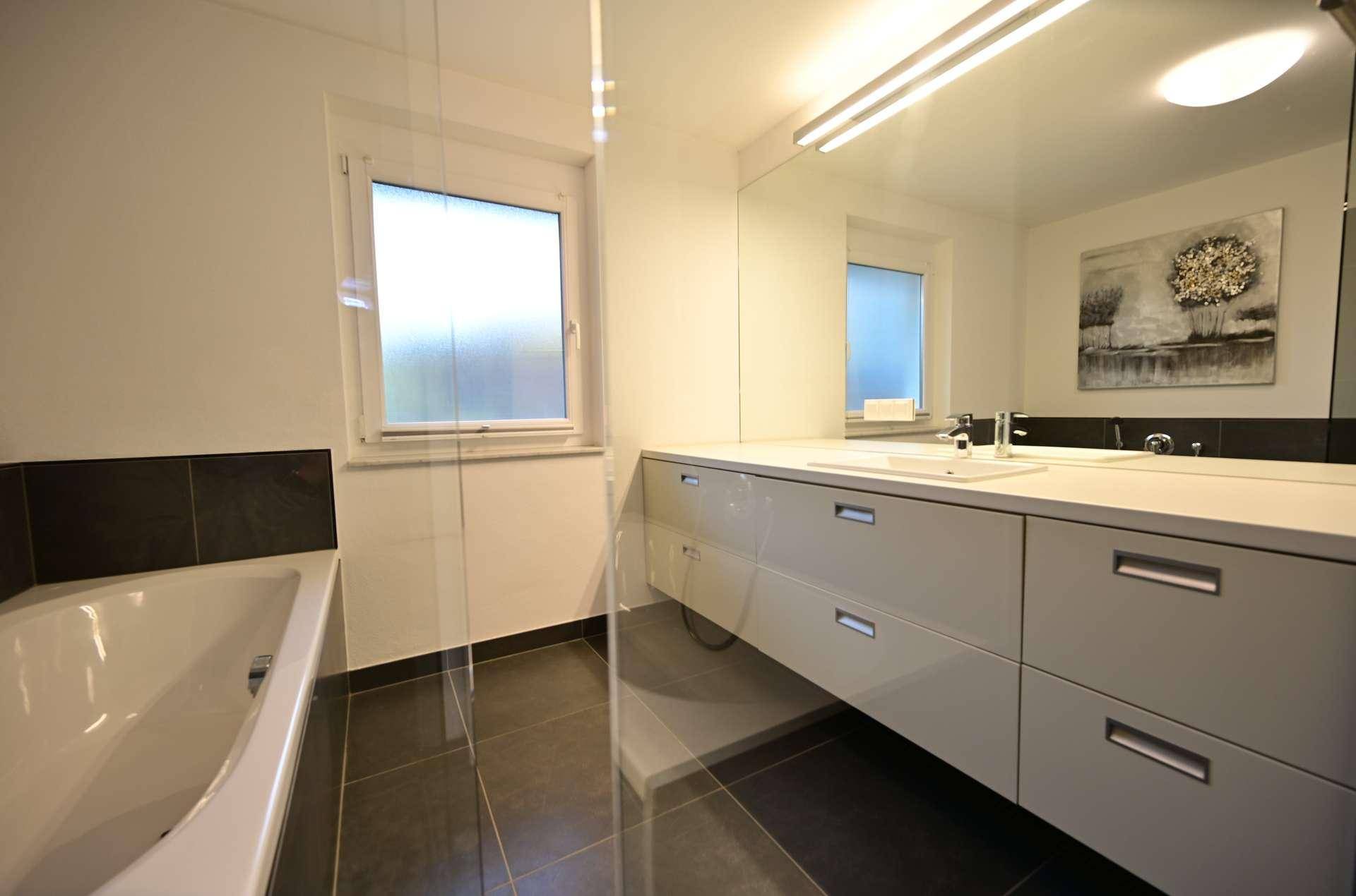 Modernes Badezimmer mit Badewanne, großem Waschtisch und Fenster für Tageslicht.