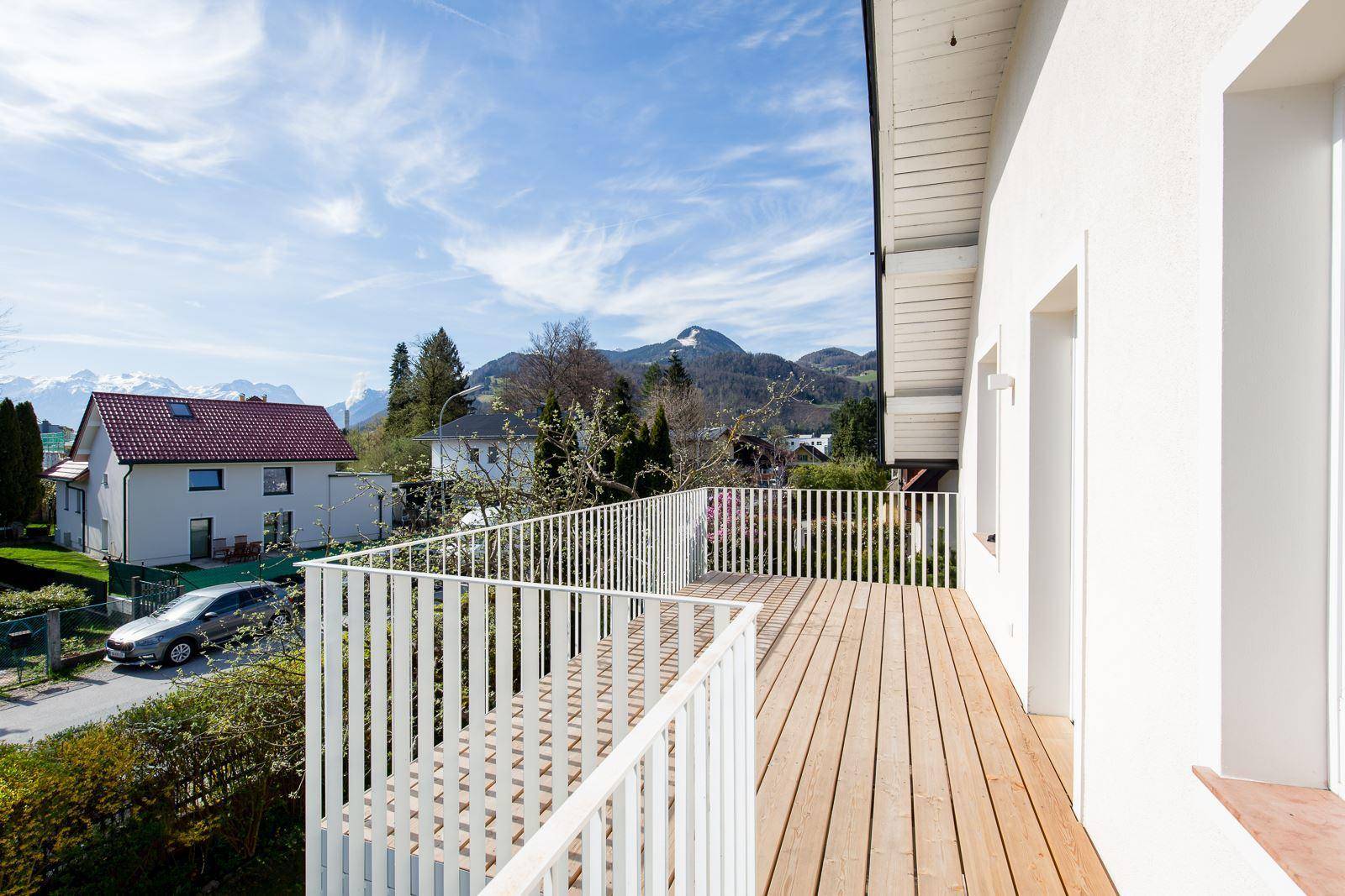 Großer Holzbalkon mit weißem Geländer und weitem Blick auf die umliegende Landschaft und Berge.