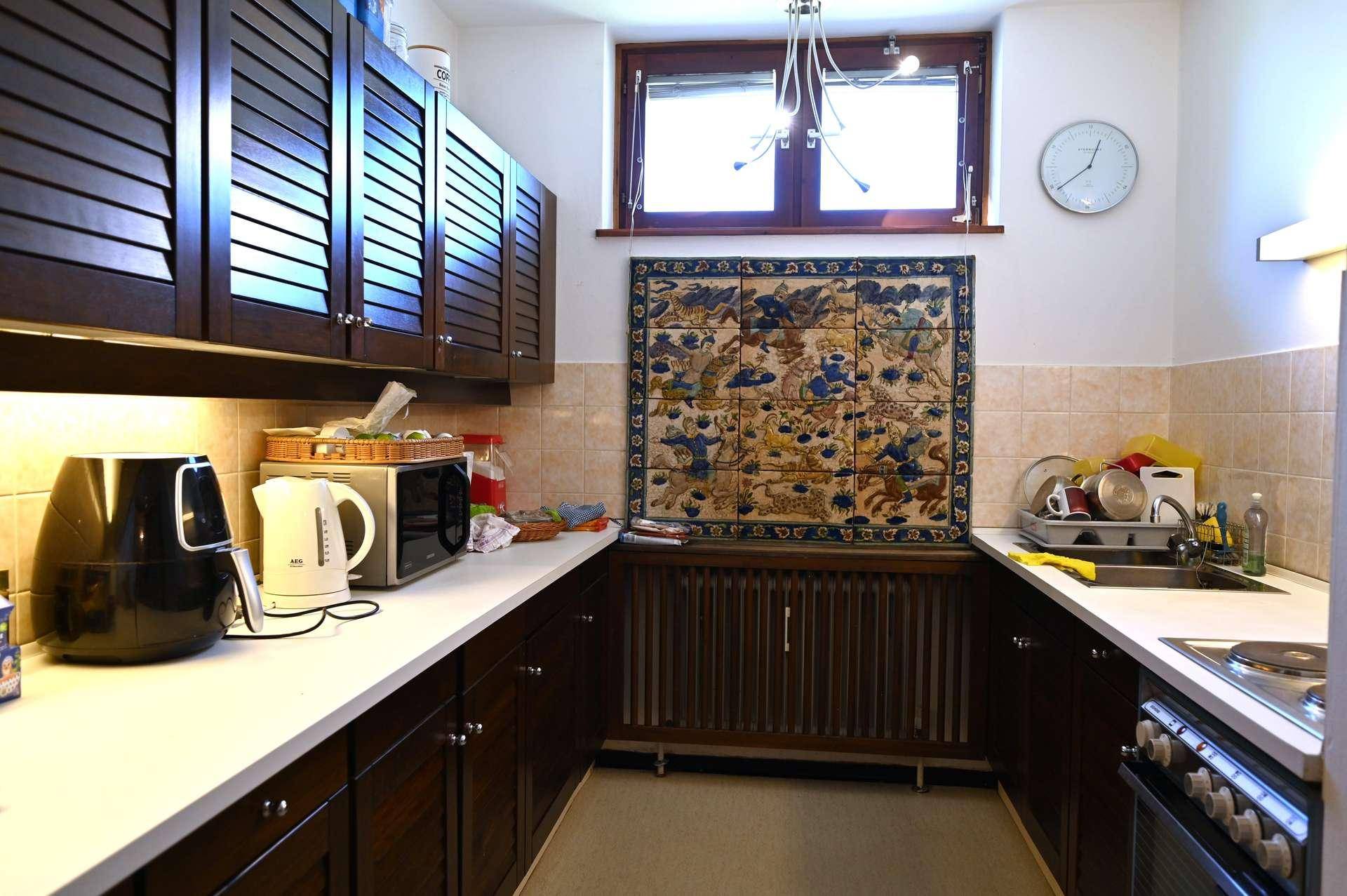 Funktionale Küche mit dunklen Holzschränken, weißer Arbeitsplatte und Fenster für Tageslicht.