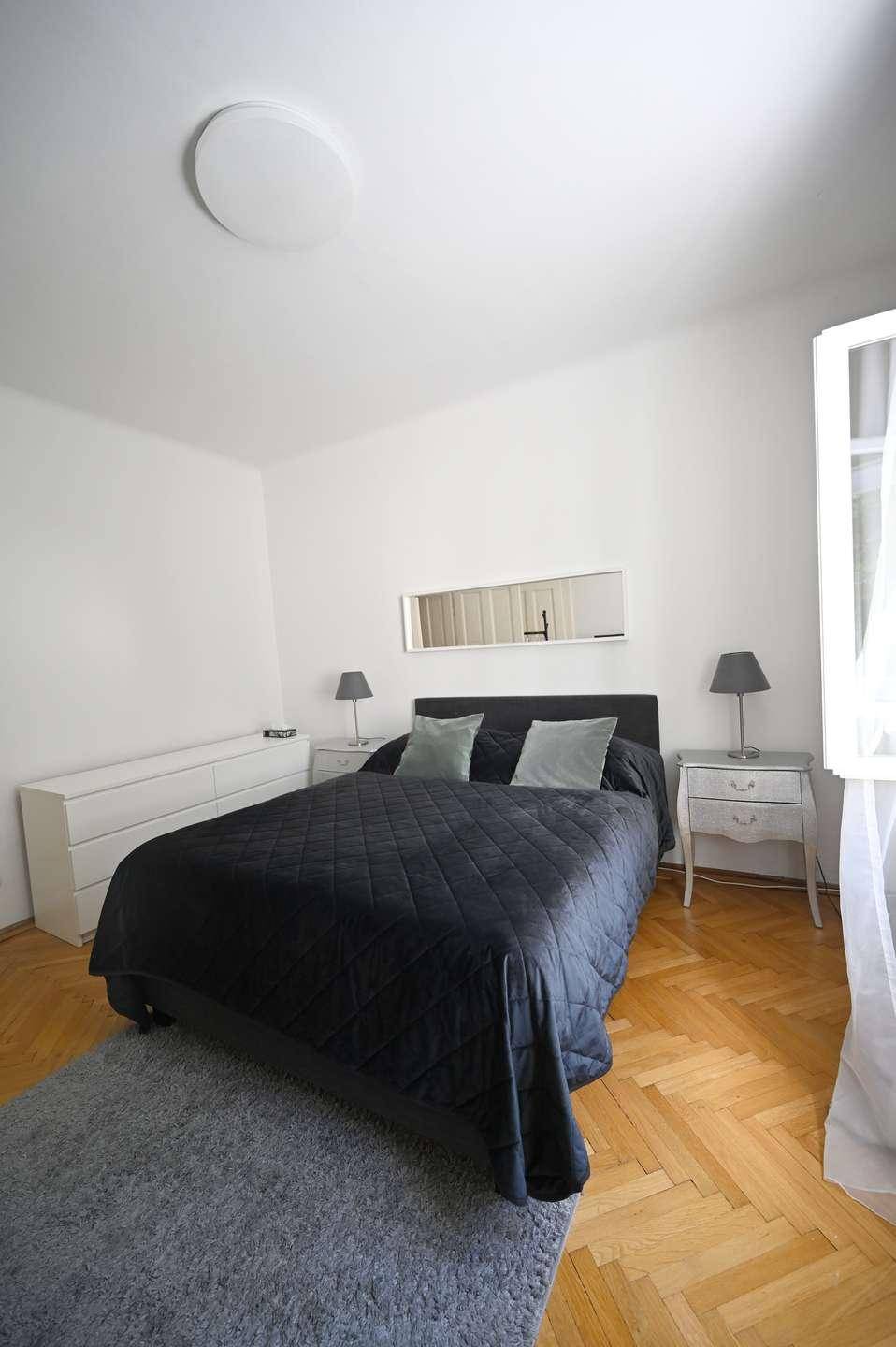 Helles Schlafzimmer mit Doppelbett, weißer Kommode und klassischem Fischgrätparkett.