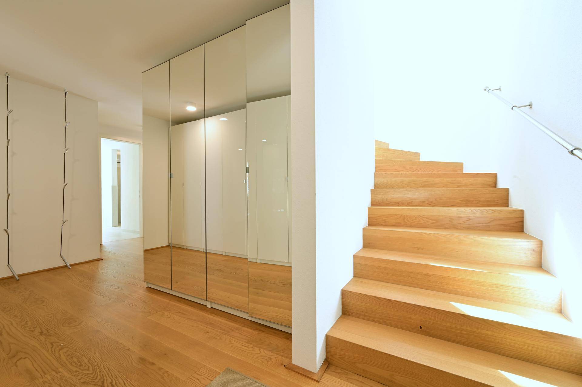 Heller Flur mit Holztreppe, integrierten Spiegelschränken und durchgehendem Parkettboden.