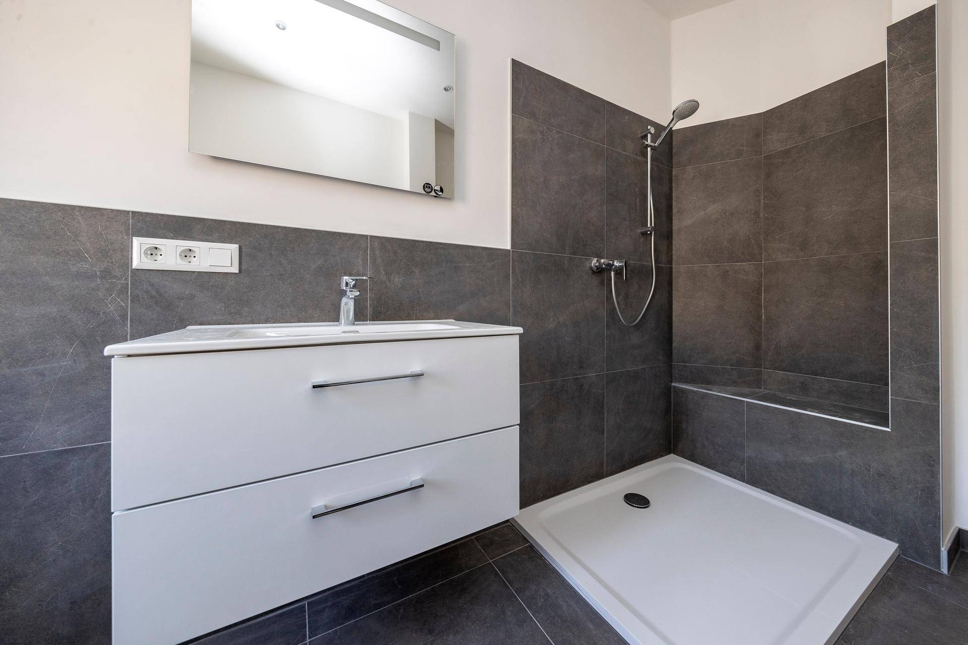 Detailansicht des modernen Badezimmers mit Waschtisch, Spiegel und geräumiger begehbarer Dusche.