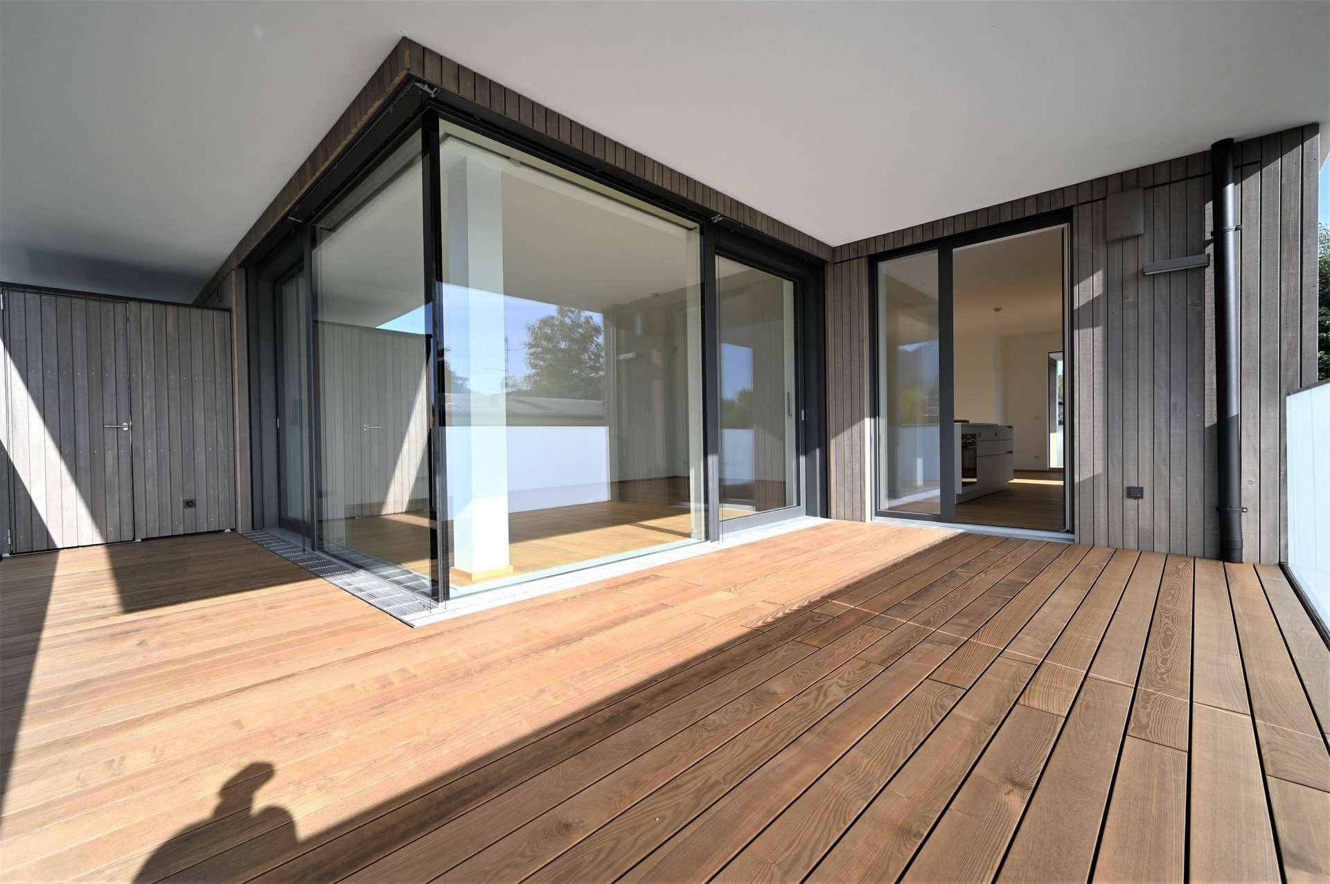 Geräumige Holzterrasse mit moderner Holzfassade und großen Glasfronten, die viel Licht hereinlassen.