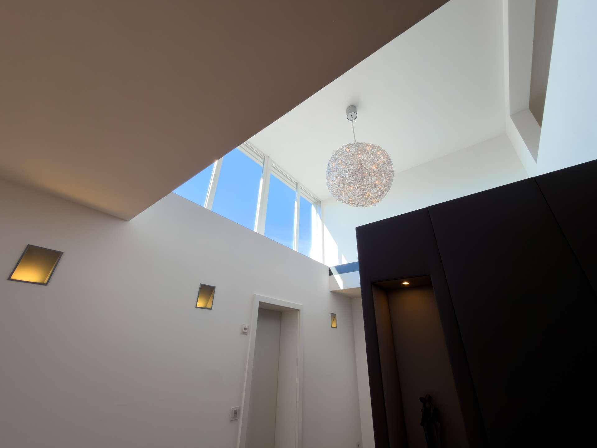 Hohe Decke mit moderner Pendelleuchte und großen Oberlichtern für reichlich Tageslicht.