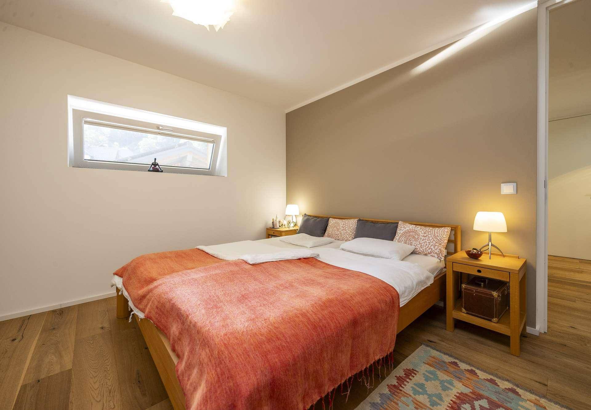 Helles Schlafzimmer mit Doppelbett, Holzboden und einem Fenster für Tageslicht.