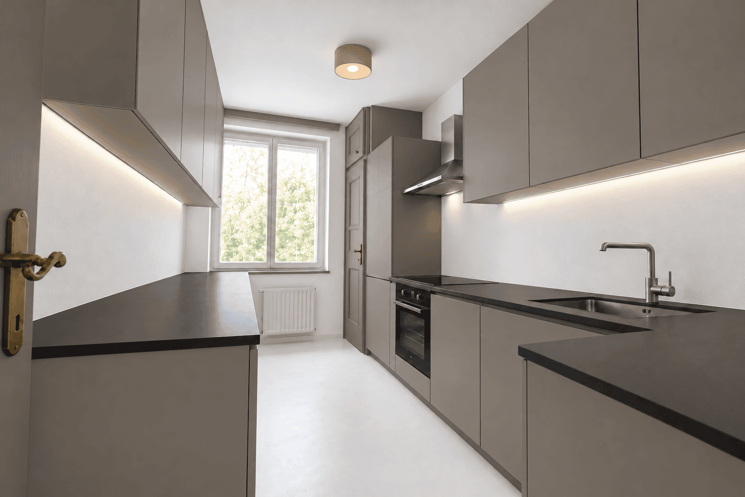 Moderne Küche mit grauen Schränken, integrierten Geräten und einem Fenster für Tageslicht.
