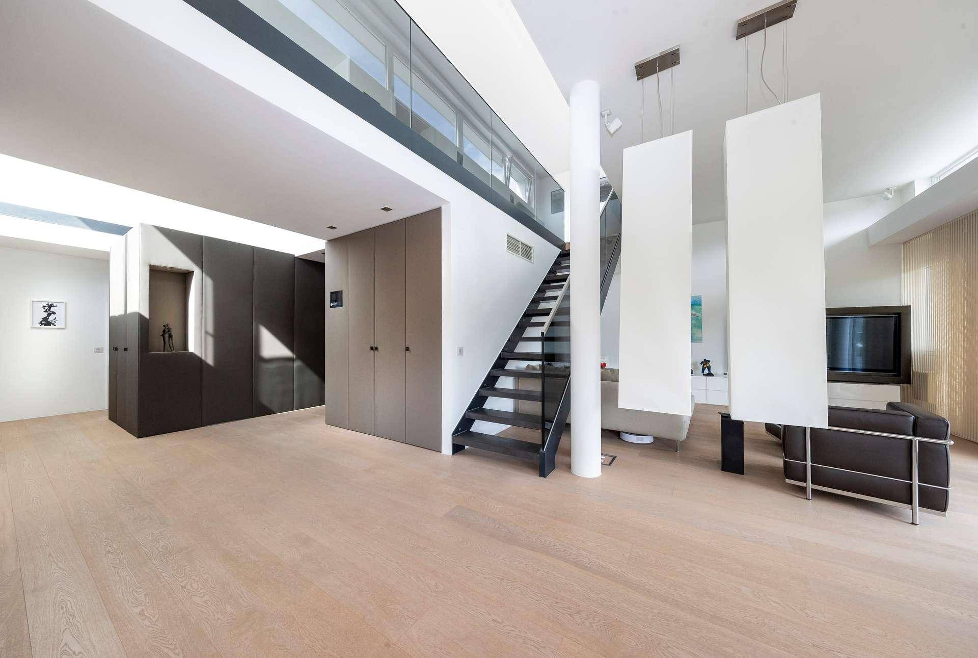 Offener Wohnbereich mit moderner Treppe, Holzboden und integrierten Schränken.