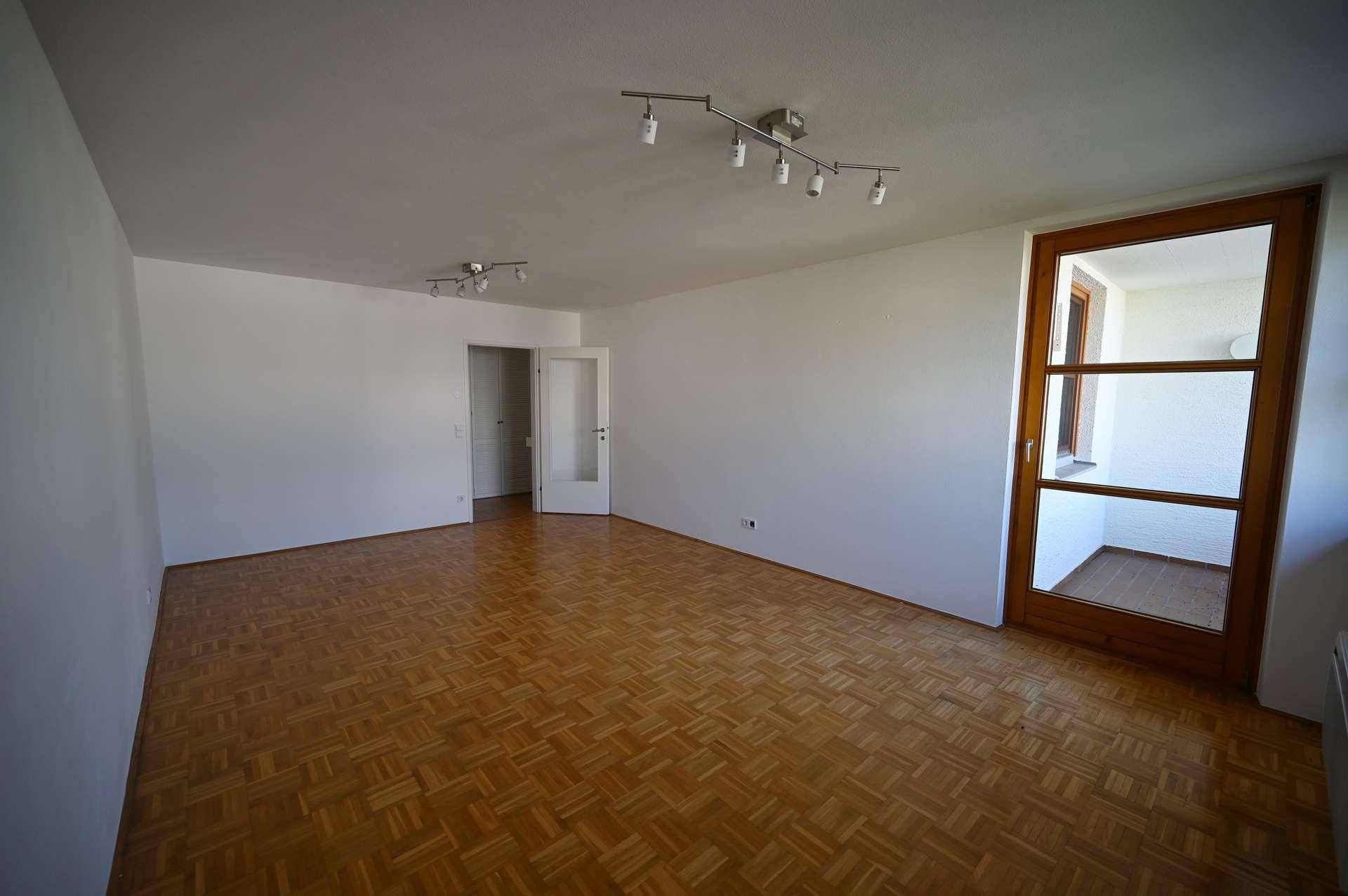 Leeres Wohnzimmer mit hellem Parkettboden und Zugang zu einem kleinen Balkon.