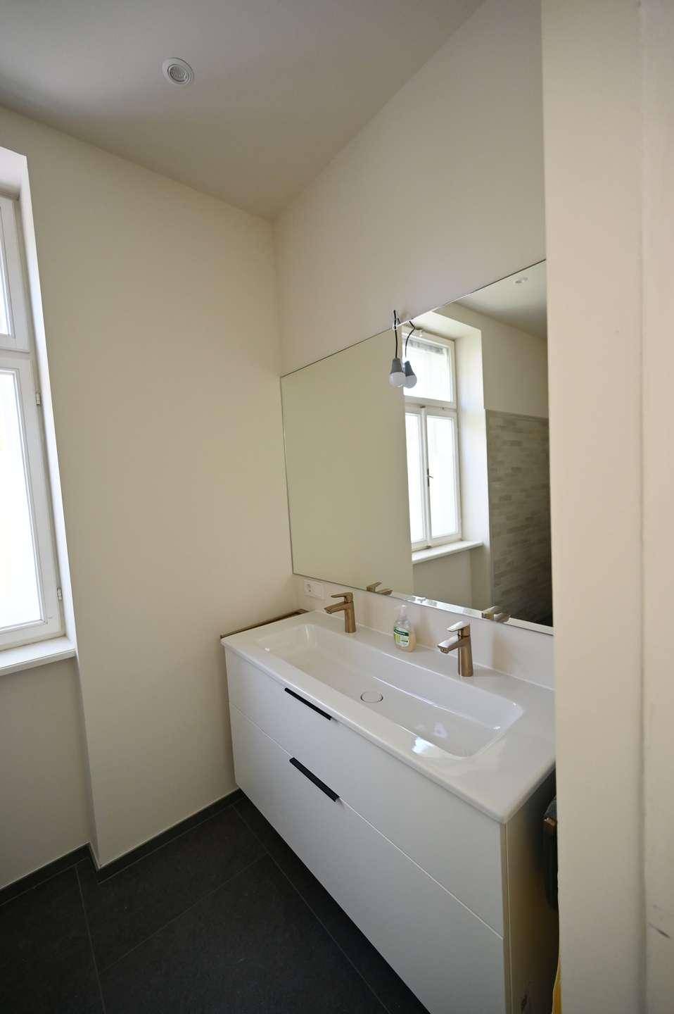 Helles Badezimmer mit Doppelwaschbecken, großem Spiegel und Fenster für Tageslicht.