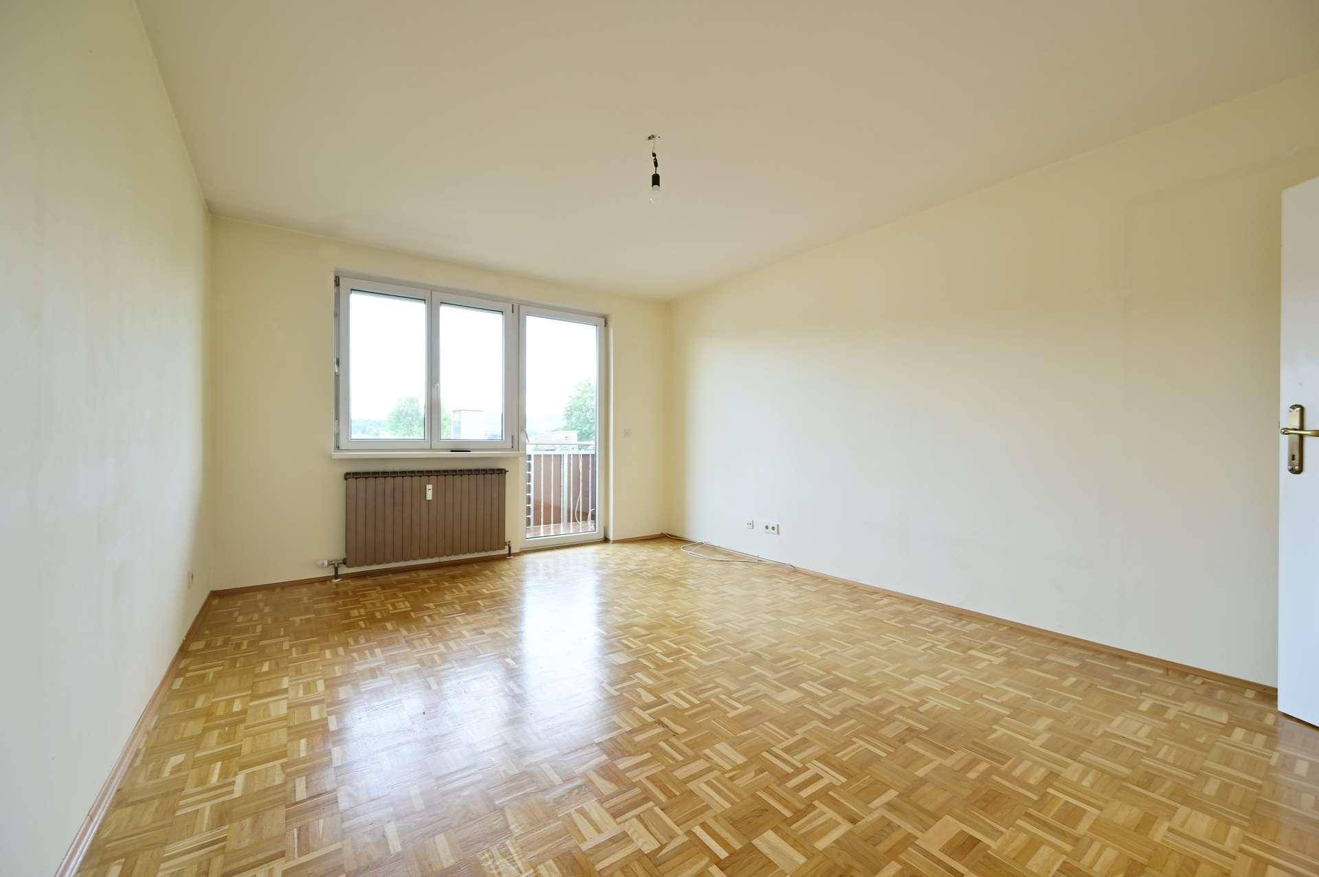 Helles Zimmer mit Parkettboden und großem Fenster, das zu einem kleinen Balkon führt.