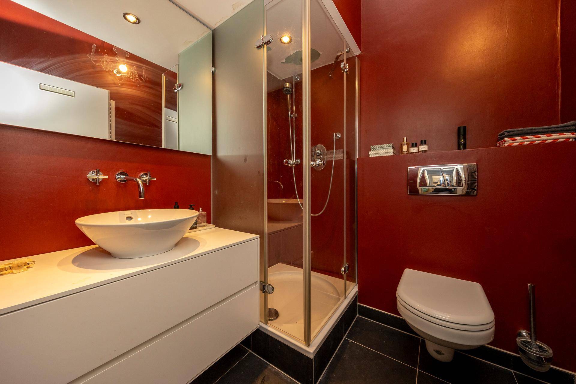 Elegantes Badezimmer mit begehbarer Dusche, Wand-WC und modernem Waschbecken, in Rot gehalten.