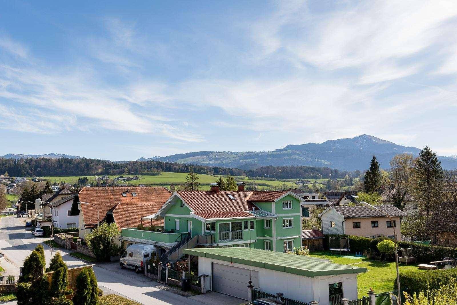 Weitläufige Wohngegend mit Häusern, grünen Feldern und beeindruckendem Bergblick.