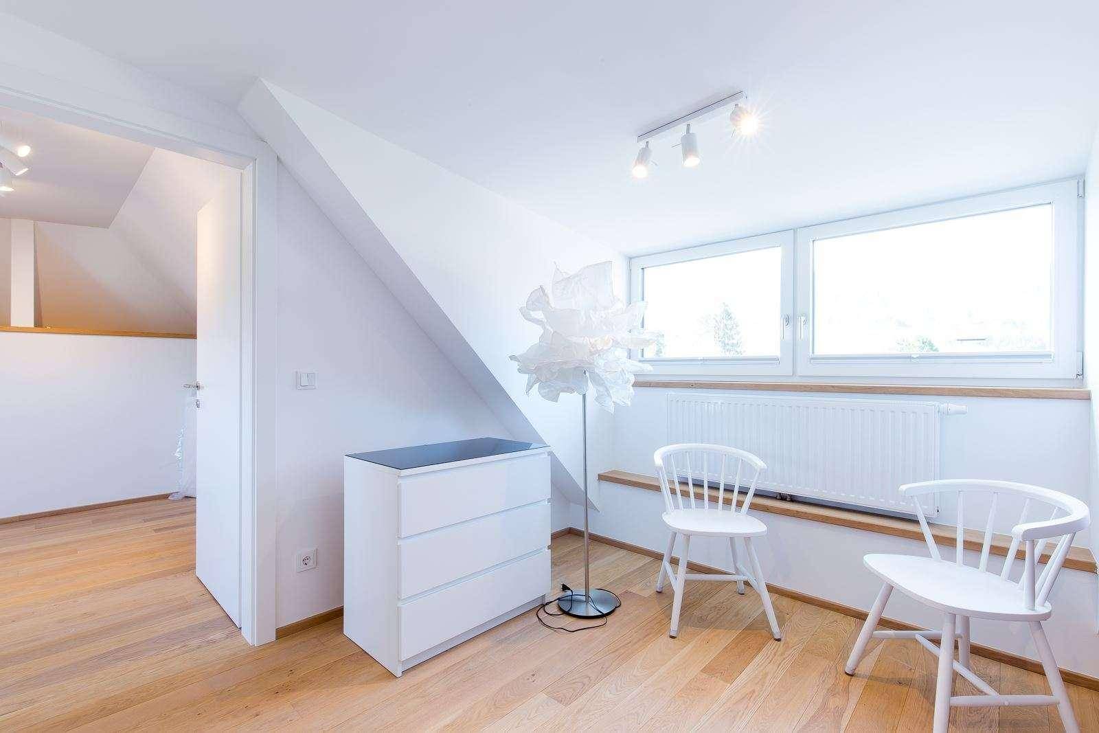 Dachgeschoss-Schlafzimmer mit schrägen Wänden, Kommode und viel Tageslicht durch die Fenster.