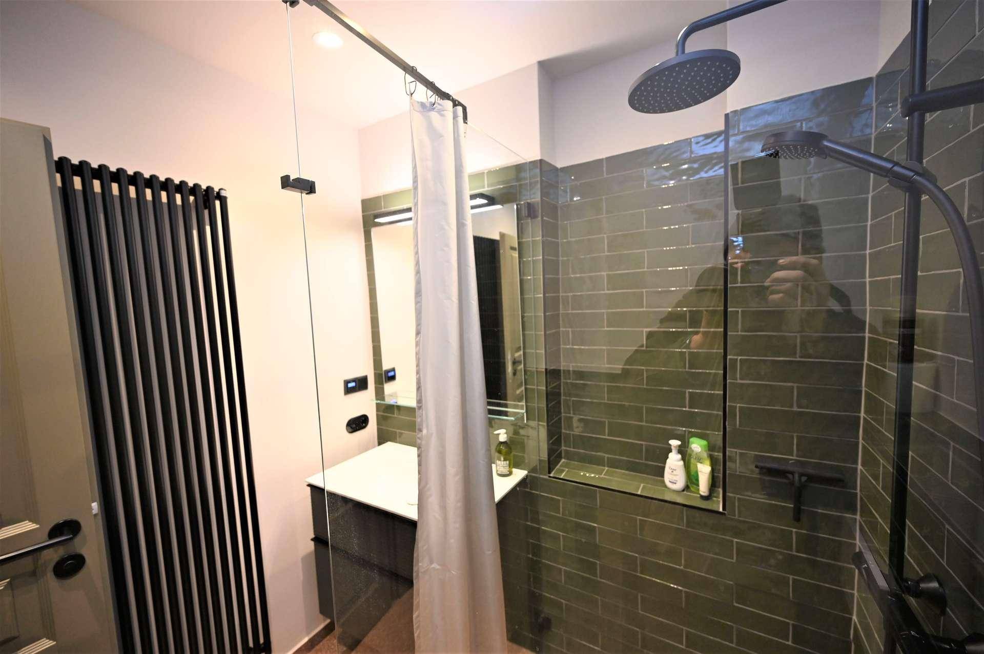 Modernes Badezimmer mit begehbarer Dusche, Waschtisch und schwarzem Heizkörper.