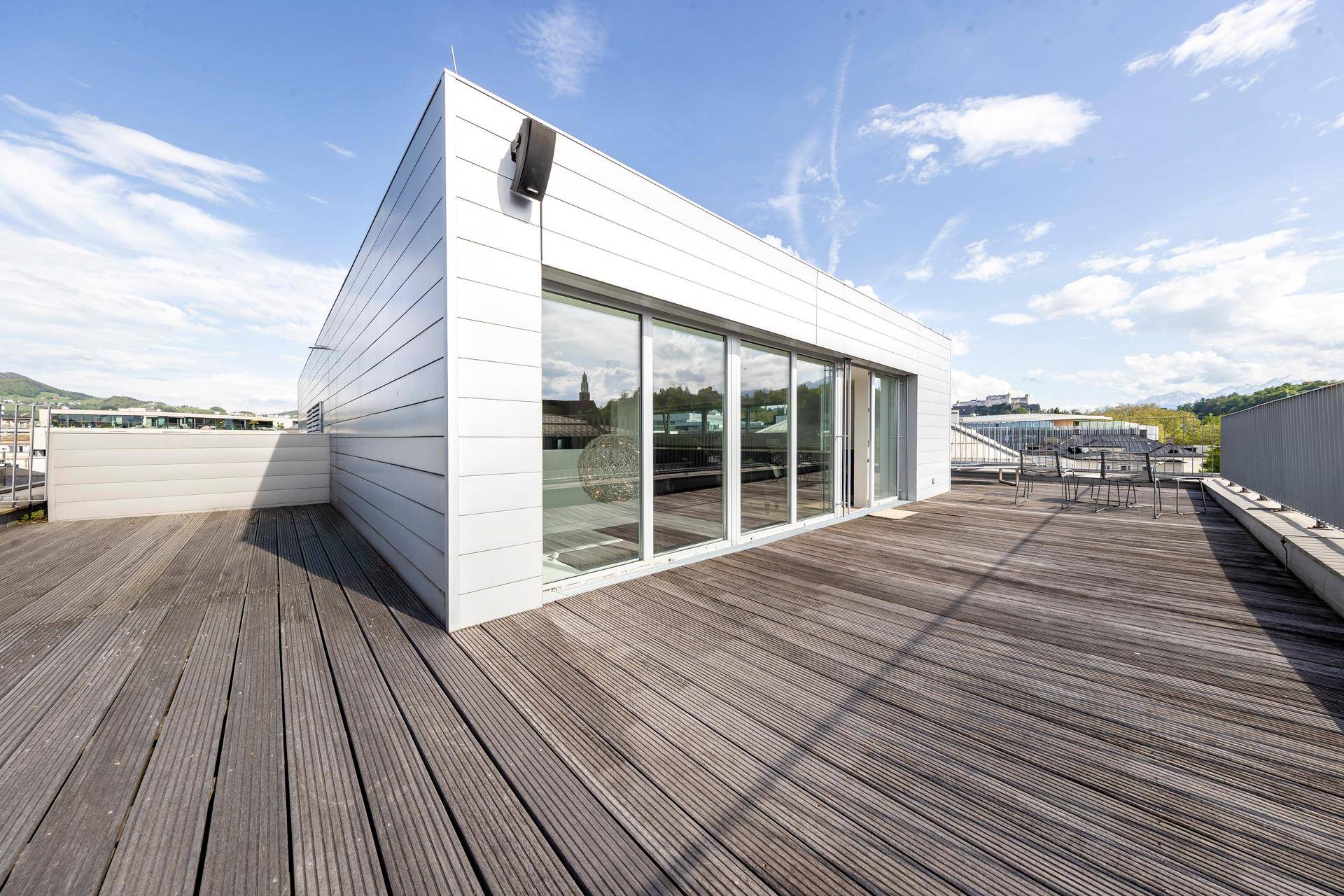 Weitläufige Dachterrasse mit Holzboden und moderner Architektur unter blauem Himmel.