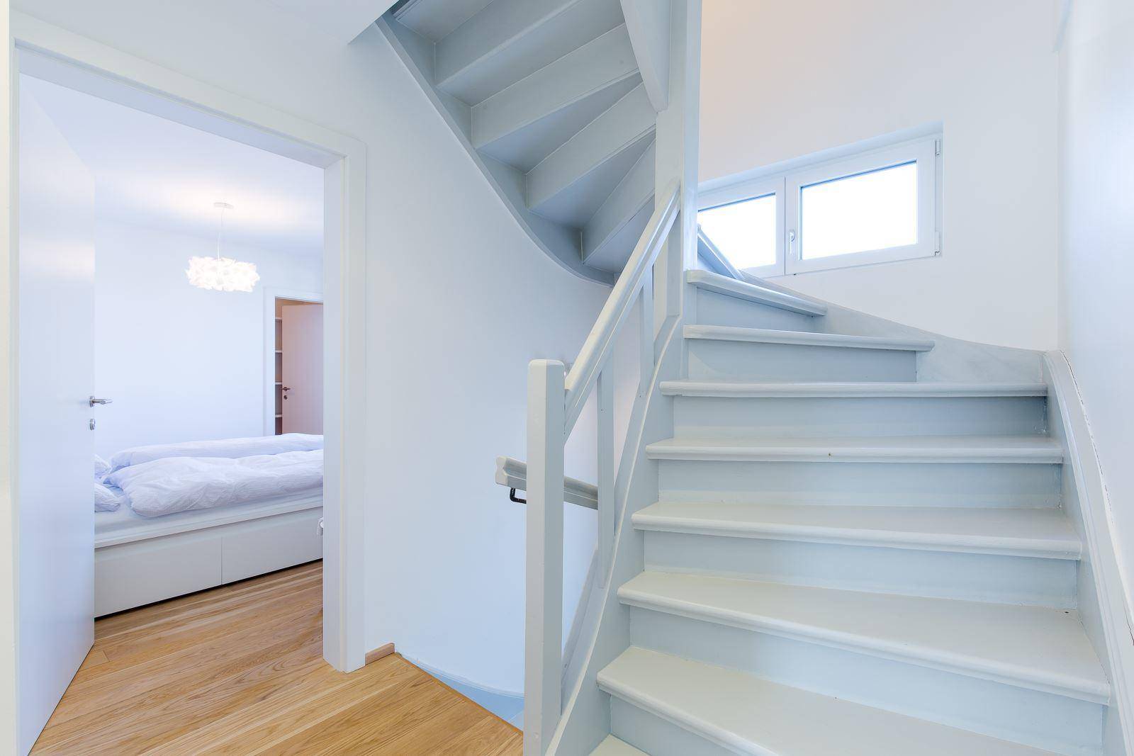 Heller Treppenaufgang mit Holzstufen und Blick in ein angrenzendes Schlafzimmer.