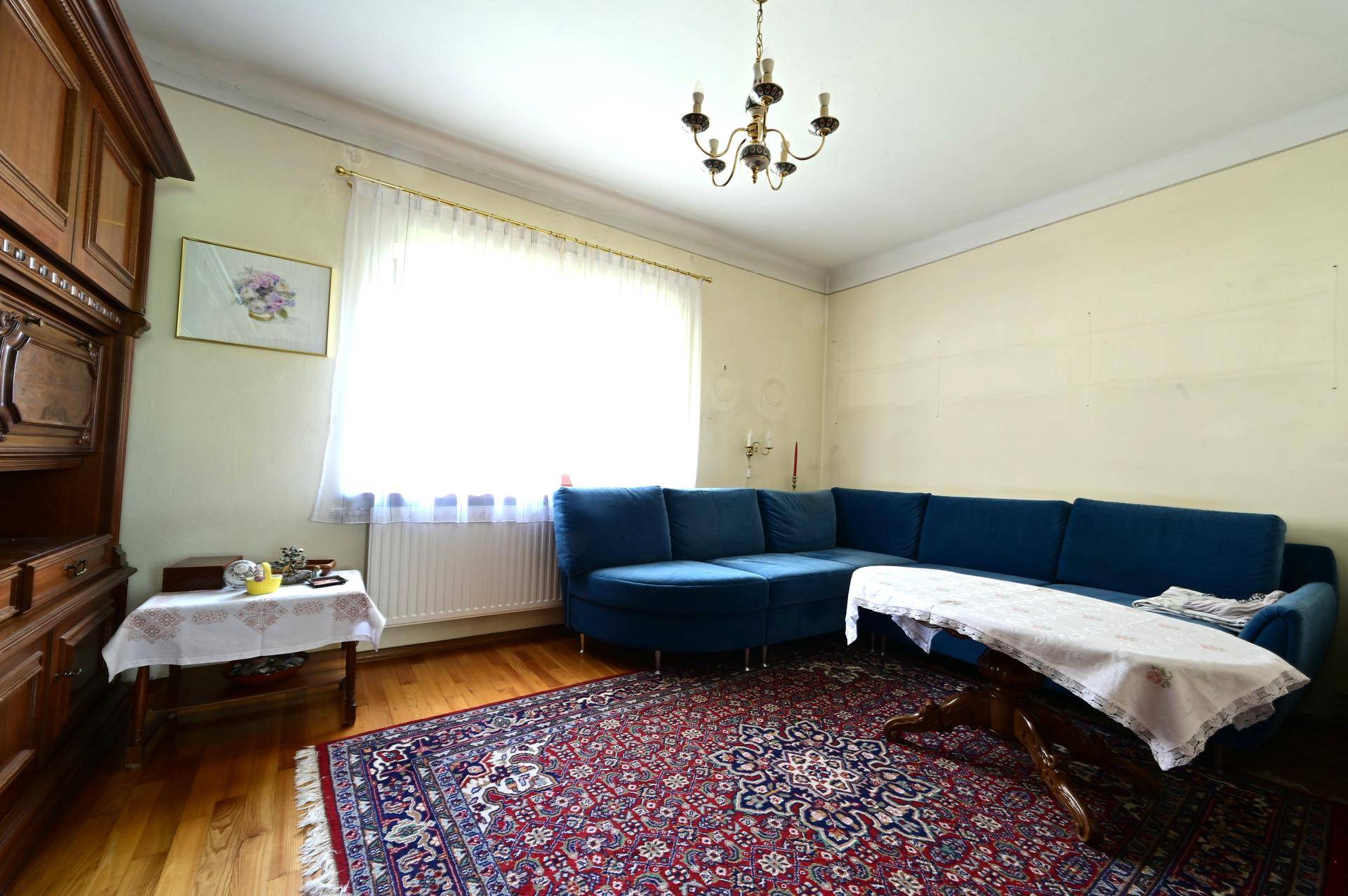 Helles Wohnzimmer mit blauem Ecksofa, Teppich, Holzboden und großen Fenstern.
