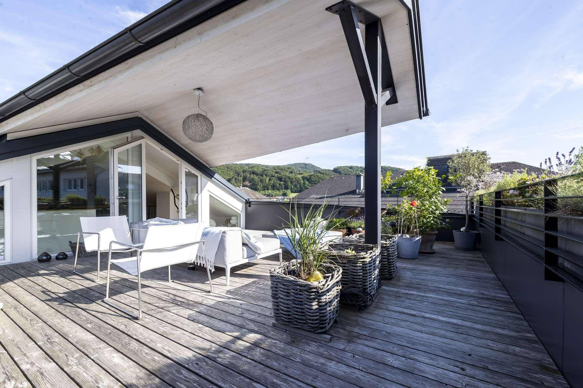 Weitläufige Dachterrasse mit Holzboden, Pflanzen und einem weiten Blick über die Umgebung.