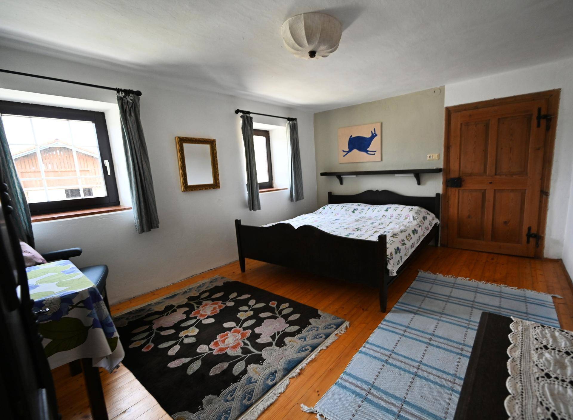 Helles Schlafzimmer mit Dielenboden, zwei Fenstern und einfacher, traditioneller Einrichtung.
