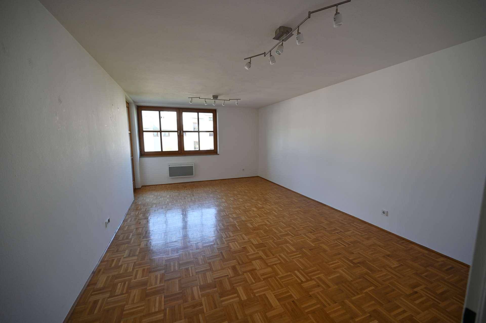 Heller Raum mit Parkettboden und einem Fenster, das viel Tageslicht hereinlässt.