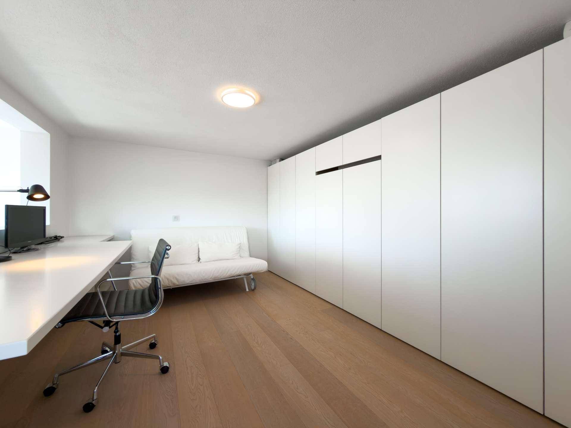 Helles Arbeitszimmer mit integrierten weißen Schränken, Schreibtisch und Holzboden.