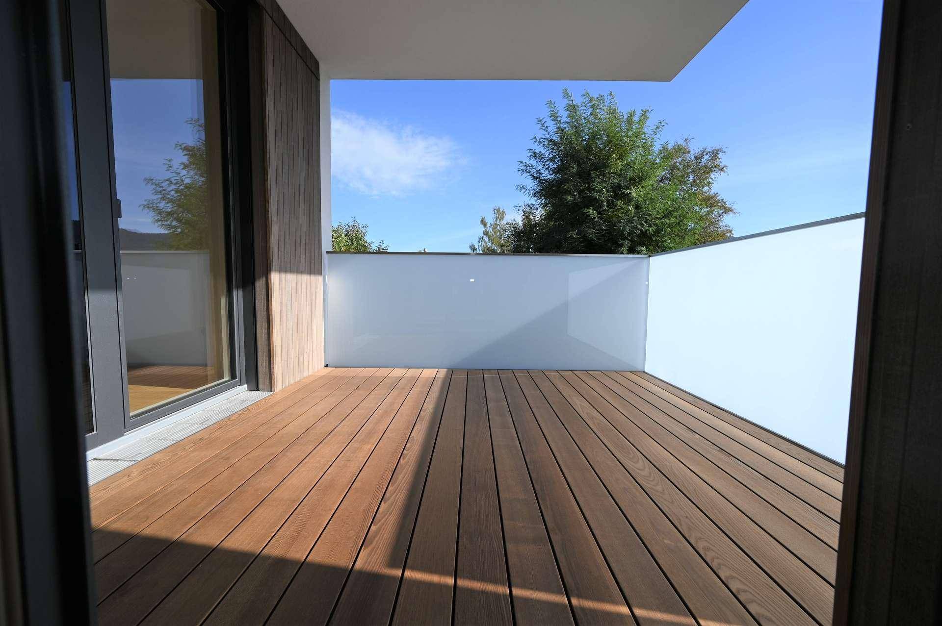 Kleiner Balkon mit Holzboden und Glasbrüstung, bietet einen sonnigen Platz im Freien.