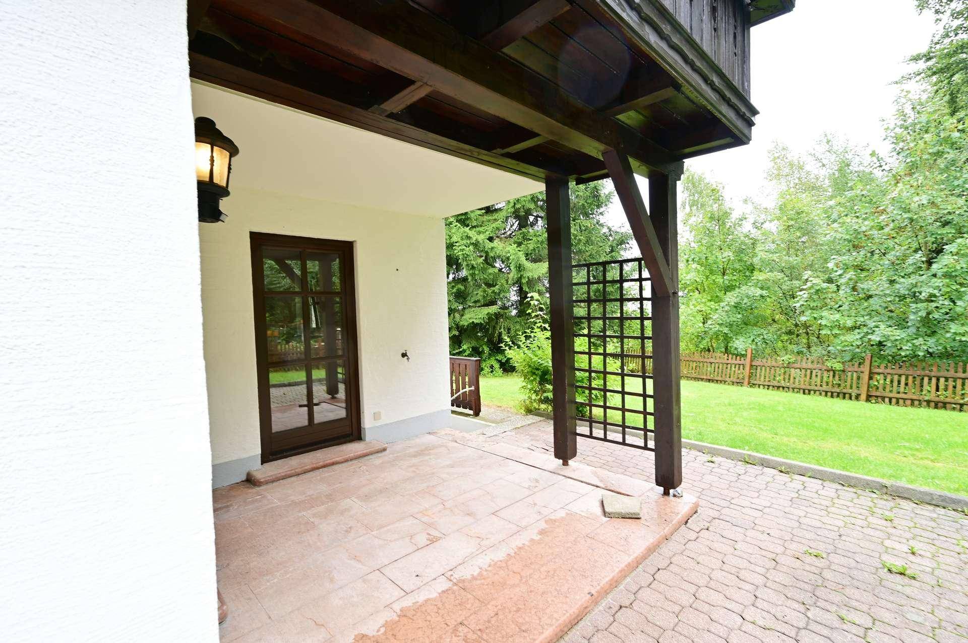 Überdachte Terrasse mit Fliesenboden und Zugang zum grünen Gartenbereich.