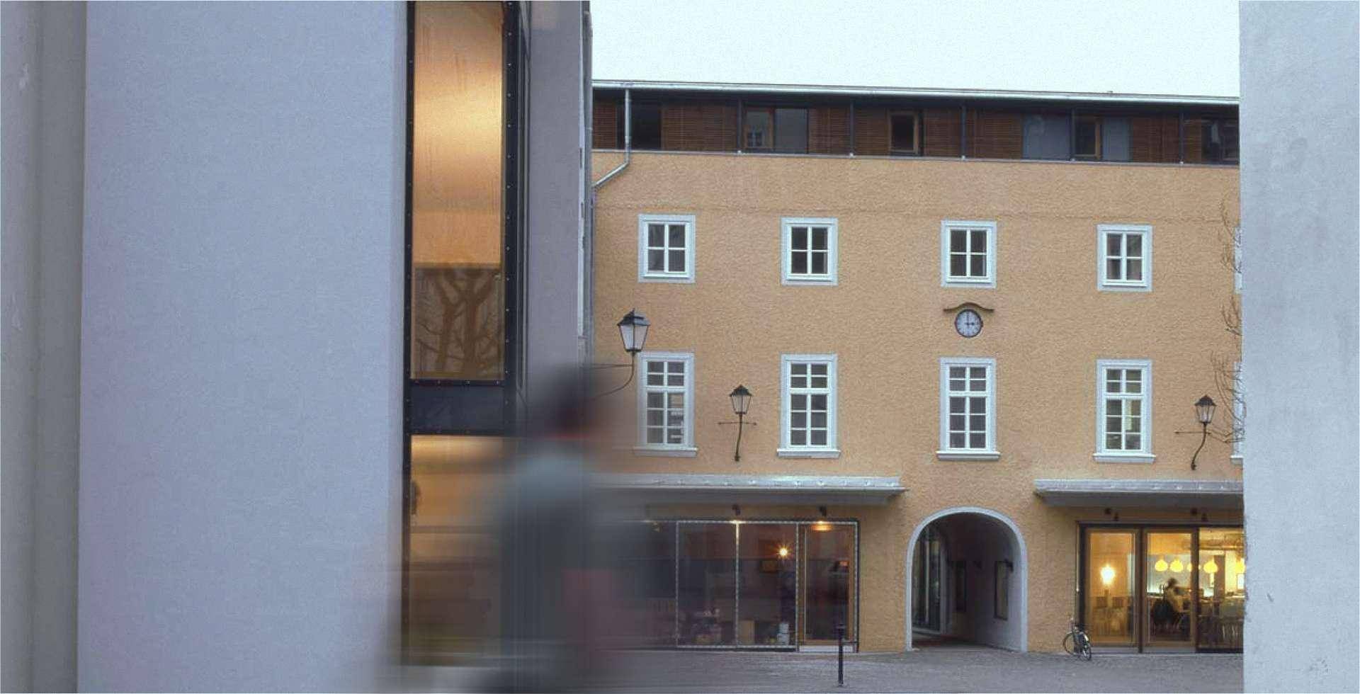 Detailansicht der modernen Fassade mit großen Fenstern und Blick auf ein traditionelles Gebäude.
