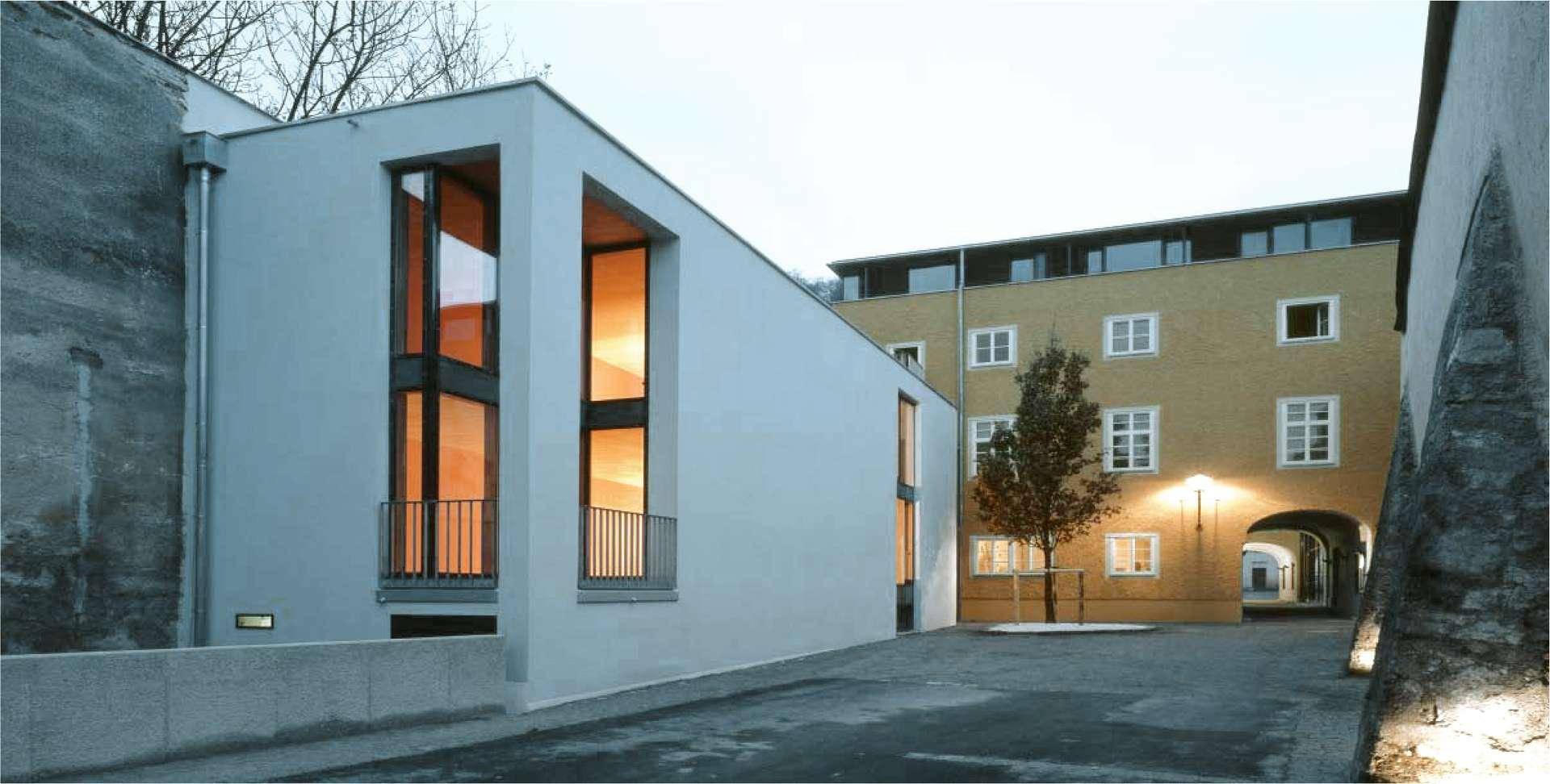 Moderne Architektur mit großen Fenstern und einem Durchgang zu einem älteren Gebäude.