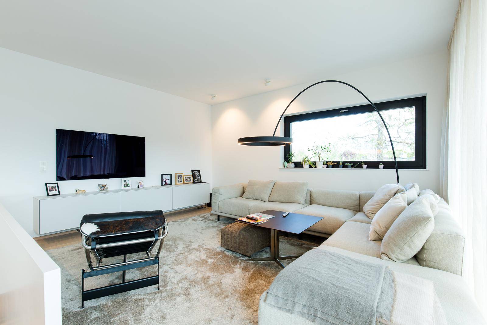 Gemütliches Wohnzimmer mit großem Sofa, Teppich und modernem Bogenlampen-Design, hell und einladend.