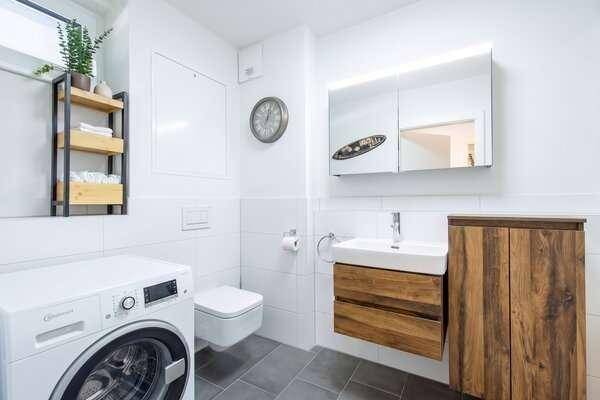 Modernes Badezimmer mit Waschmaschine, wandhängendem WC und Holzwaschtischunterschrank.