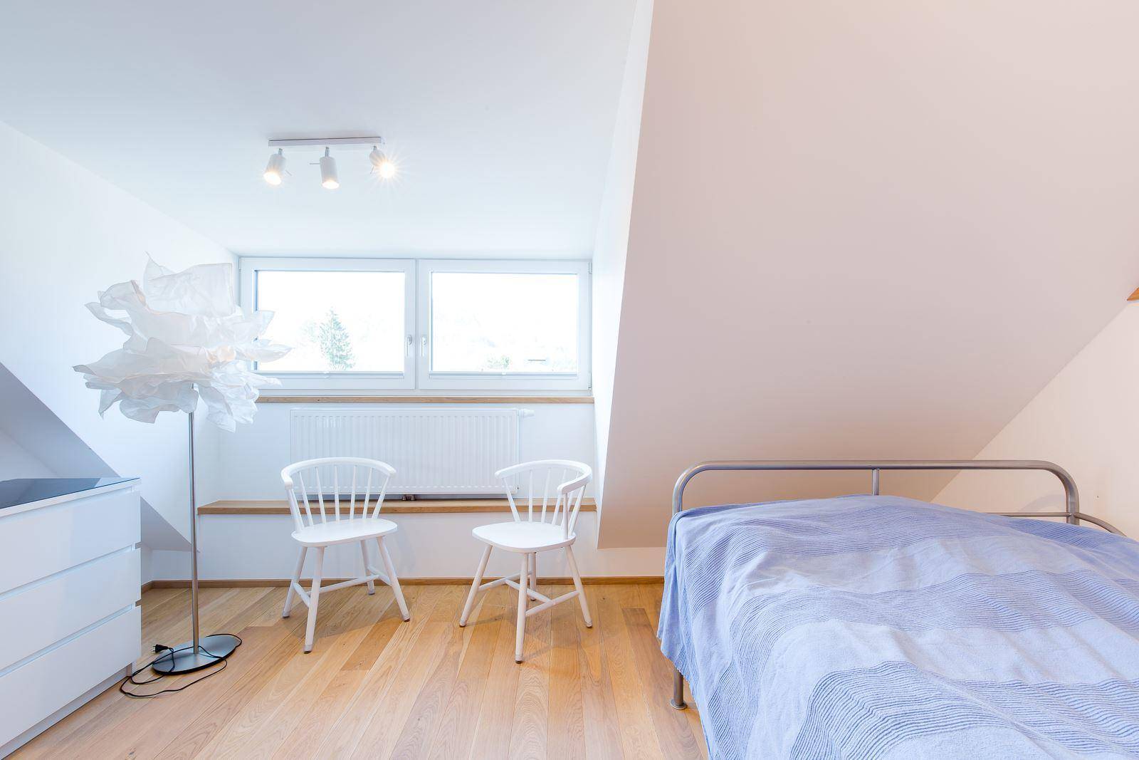 Helles Schlafzimmer im Dachgeschoss mit Holzboden, Dachschräge und großen Fenstern.