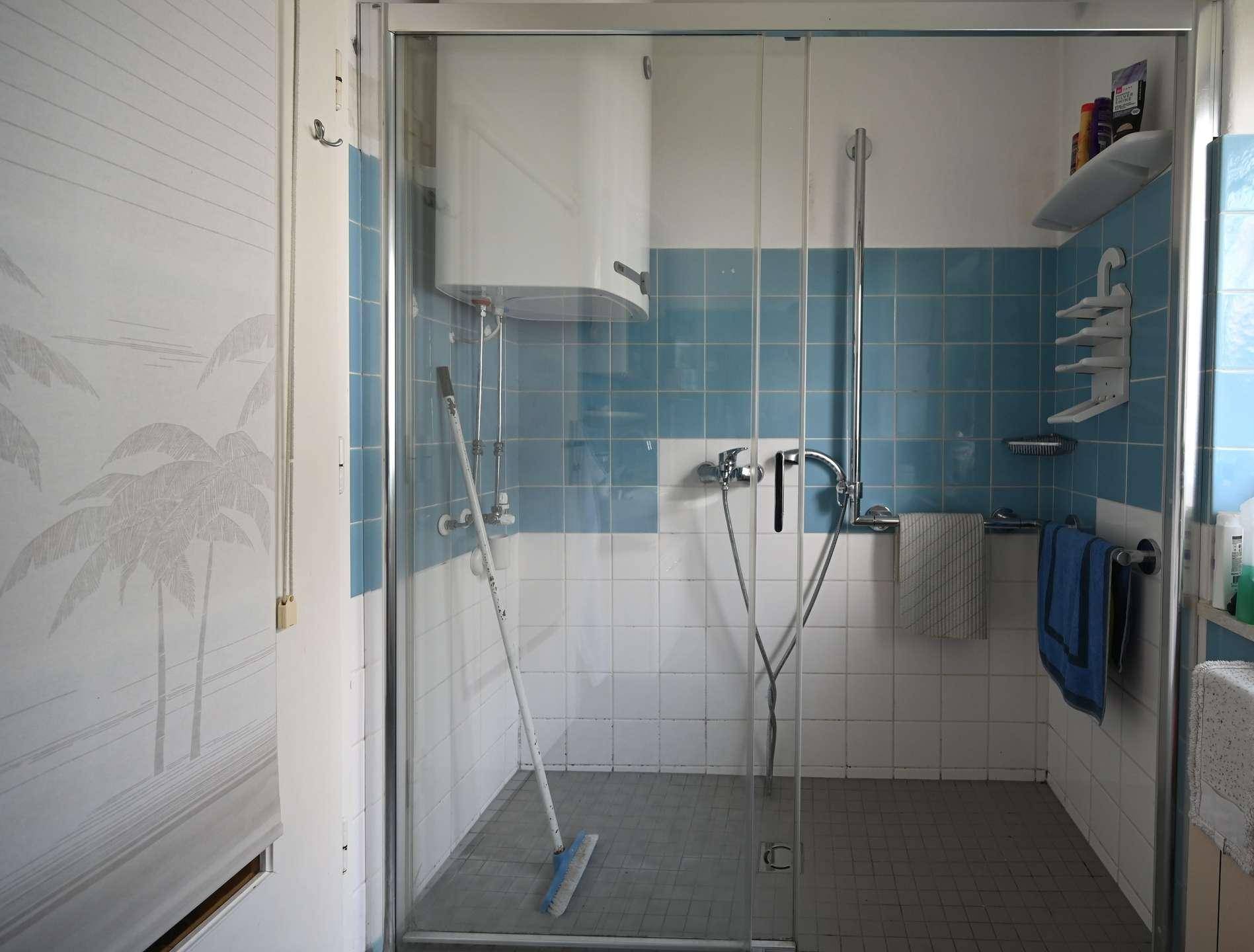 Badezimmer mit blauen und weißen Fliesen, Duschkabine und Warmwasserboiler.
