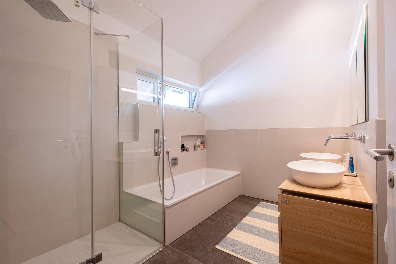 Modernes Badezimmer mit Dusche, Badewanne, Doppelwaschbecken und einem Fenster für Tageslicht.