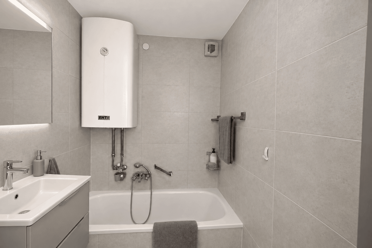 Funktionales Badezimmer mit Badewanne, Waschbecken und hellgrauen Fliesen.