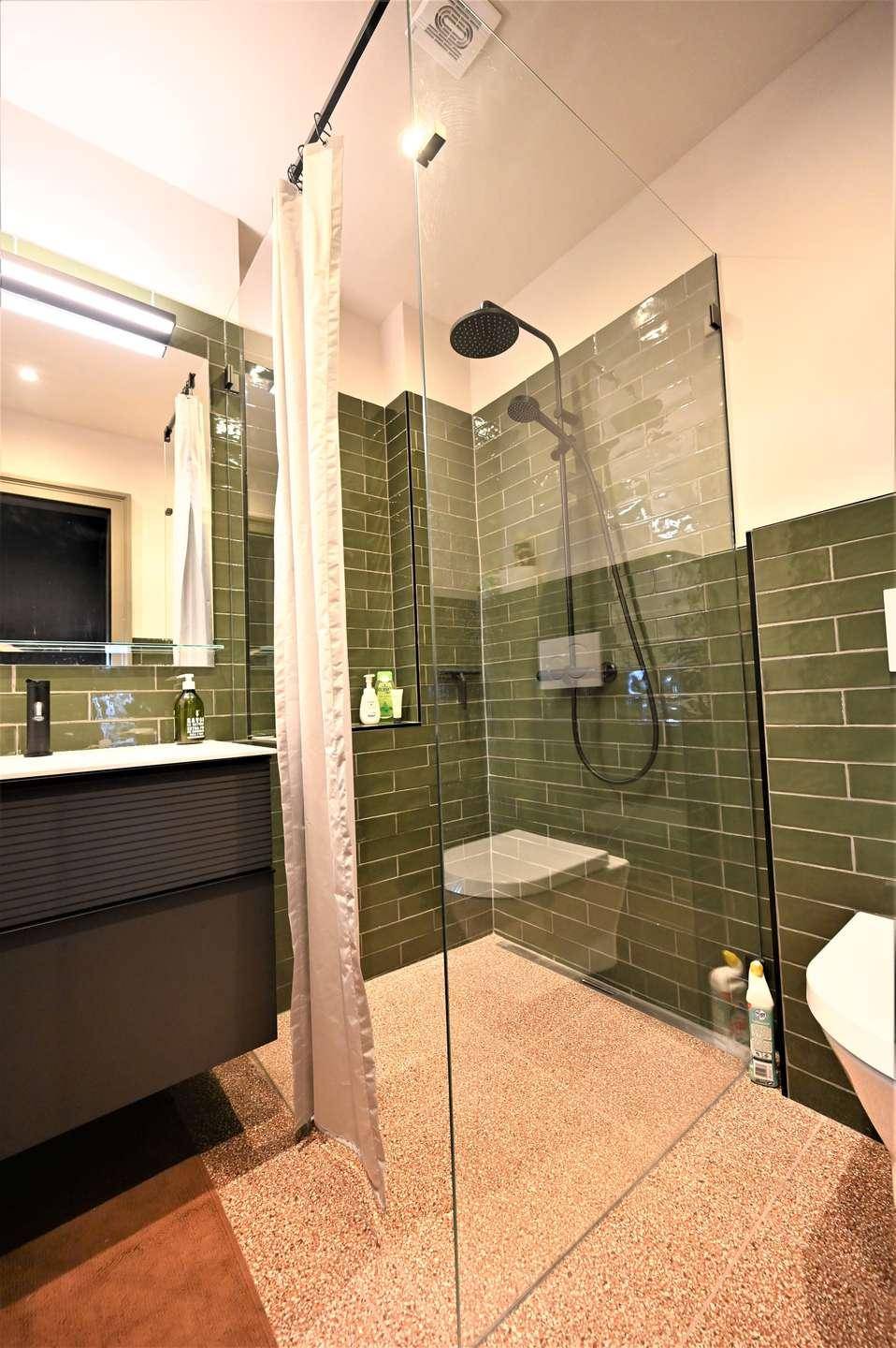 Helles Badezimmer mit begehbarer Dusche, grünen Fliesen und modernem WC.
