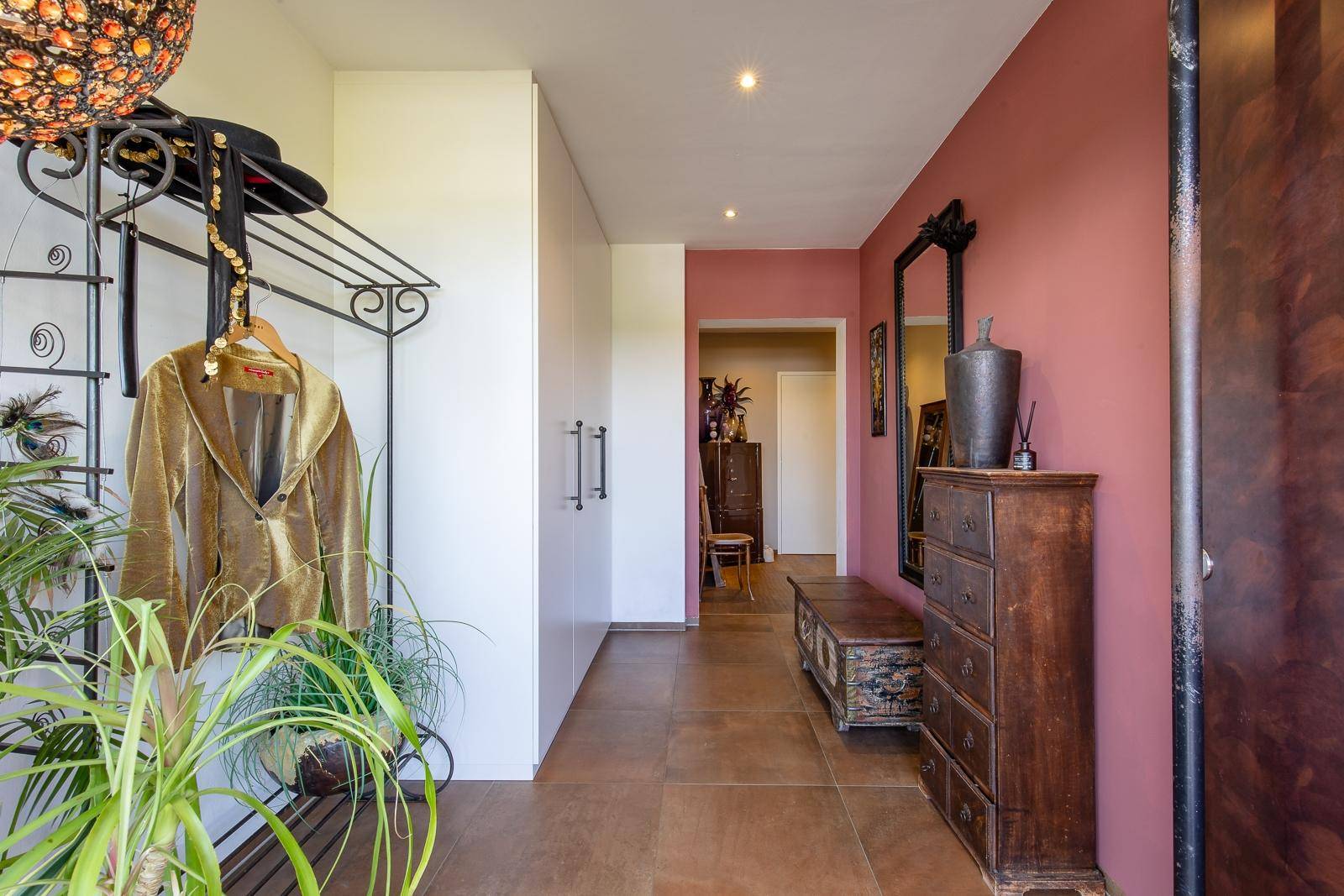 Einladender Eingangsbereich mit Terrakotta-Fliesen, Garderobe und antiken Möbeln an einer rosafarbenen Wand.