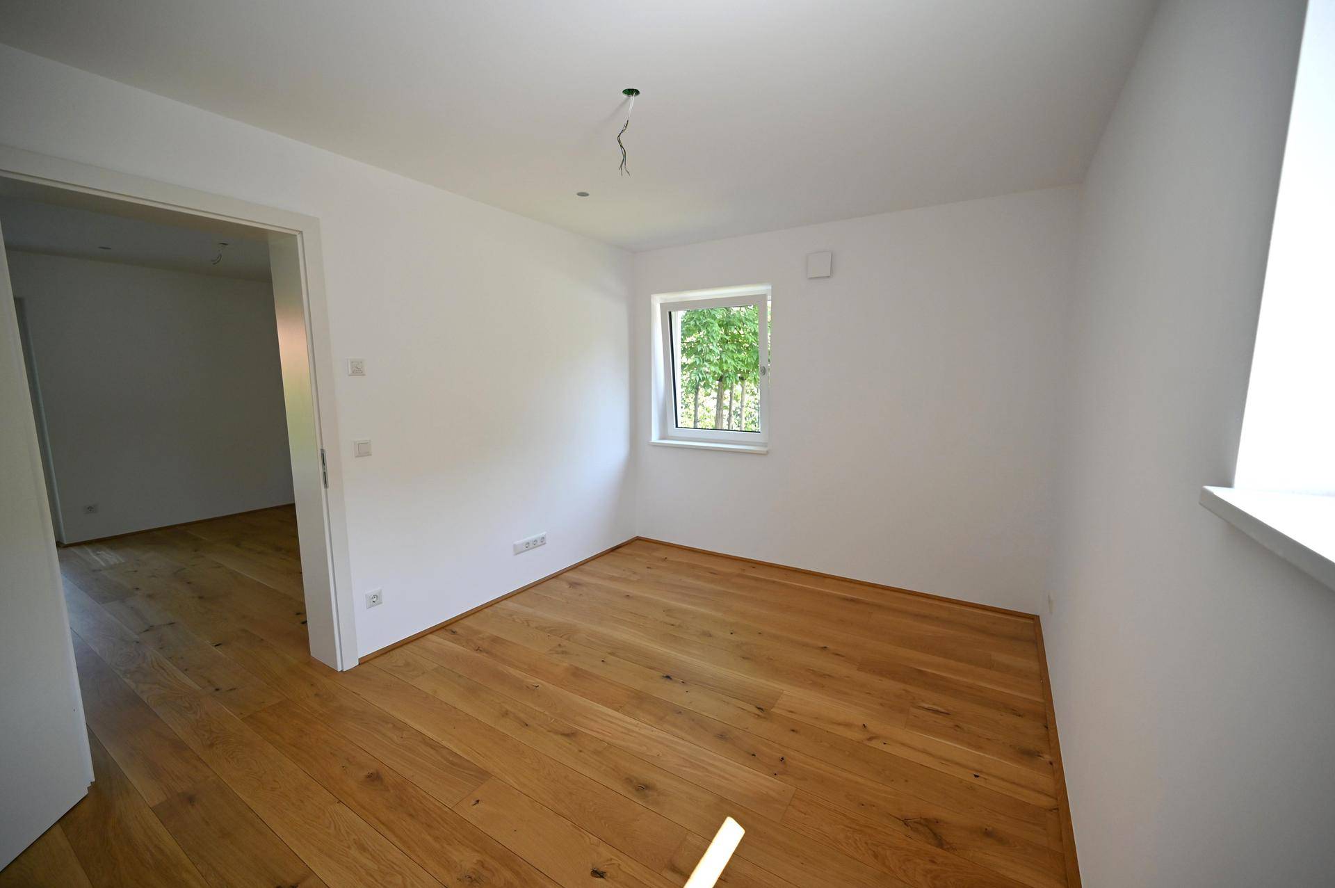 Helles Schlafzimmer mit Holzboden und einem Fenster, bereit zur individuellen Gestaltung.
