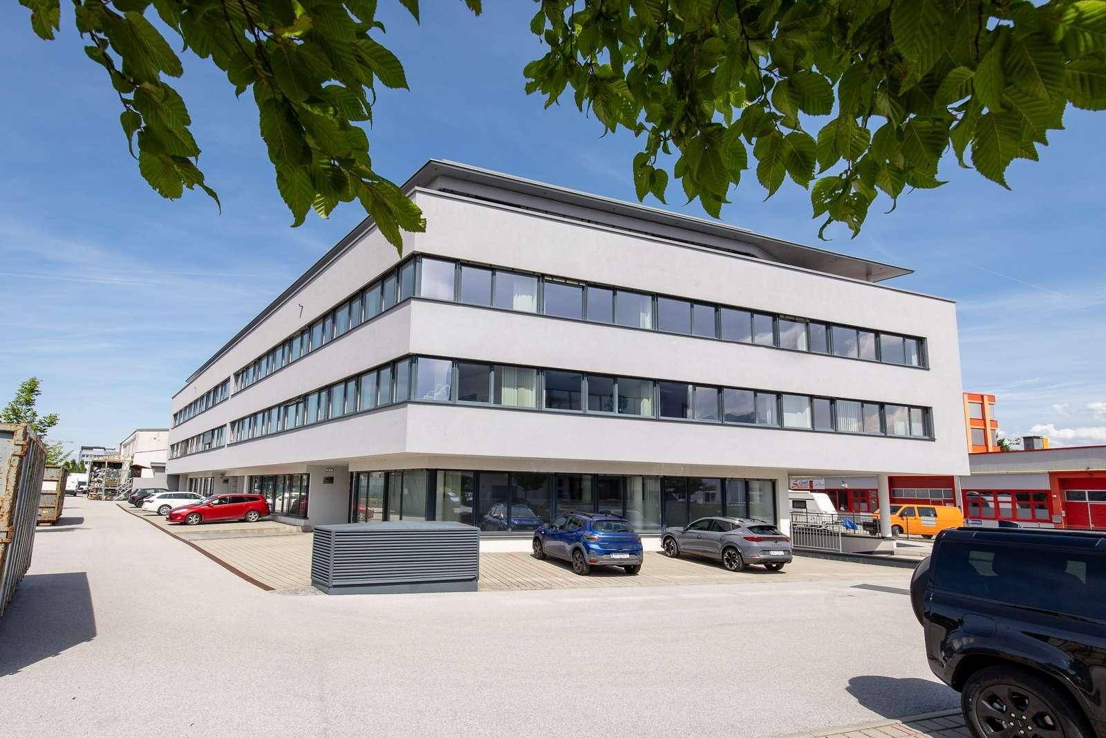 Modernes Bürogebäude mit klarer Architektur, großen Fenstern und Parkplätzen im Freien.