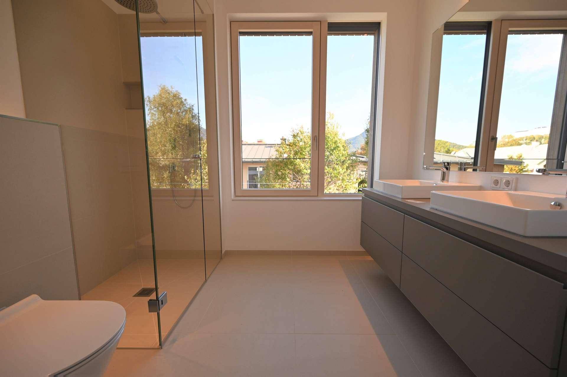 Modernes Badezimmer mit Doppelwaschbecken, großer begehbarer Dusche und Fenster für natürliches Licht.