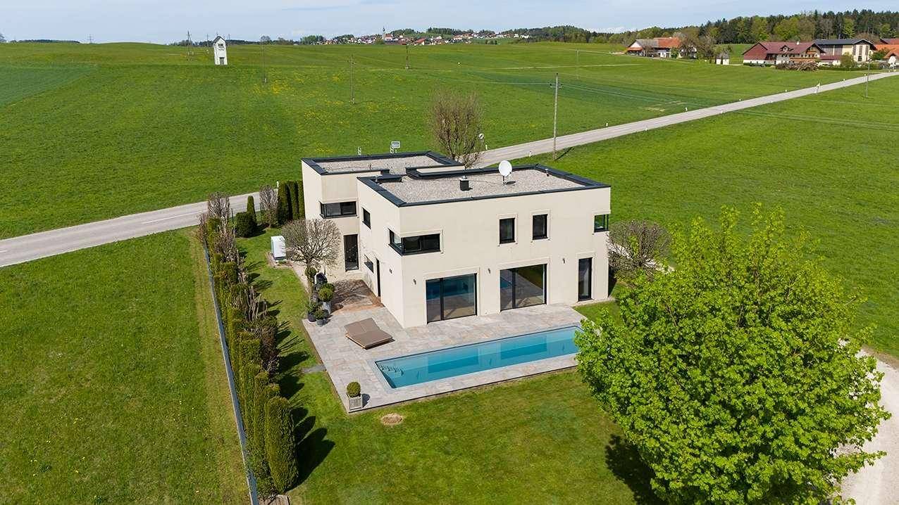 Moderne Villa mit Flachdach und Swimmingpool, umgeben von grünen Feldern und ländlicher Idylle.