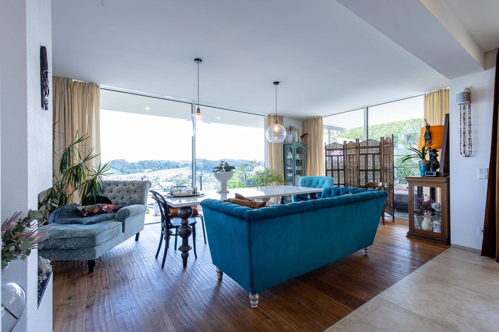 Offener Wohn- und Essbereich mit blauen Sofas, Holzboden und Panoramafenstern.