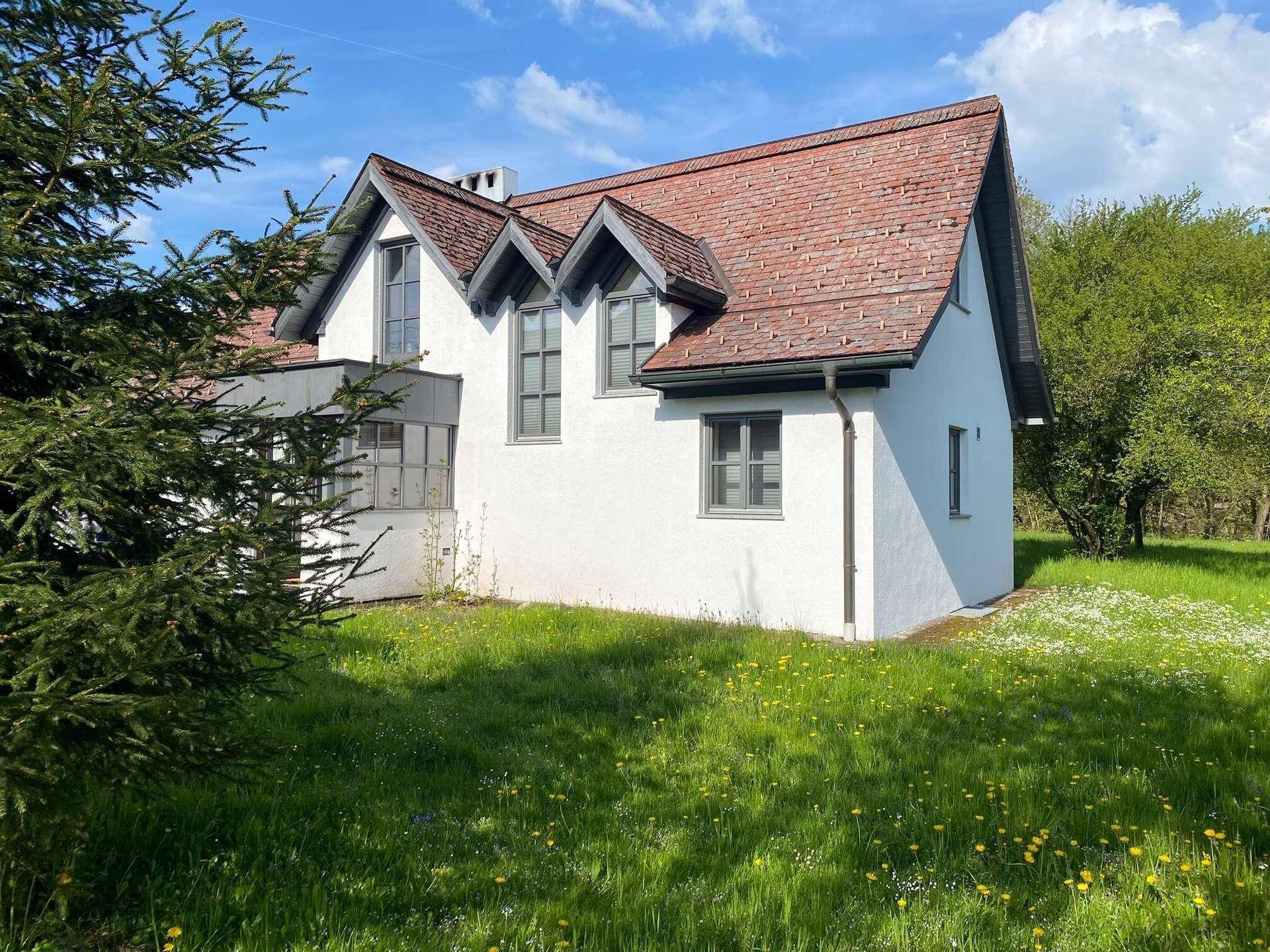 Nahaufnahme eines weißen Hauses mit rotem Ziegeldach und Gauben, umgeben von einer grünen Wiese.